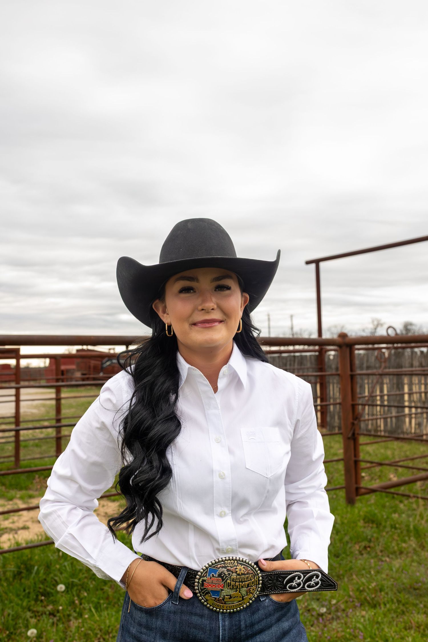 Western style portrait in white button-up shirt and black cowboy hat against rustic ranch backdrop.