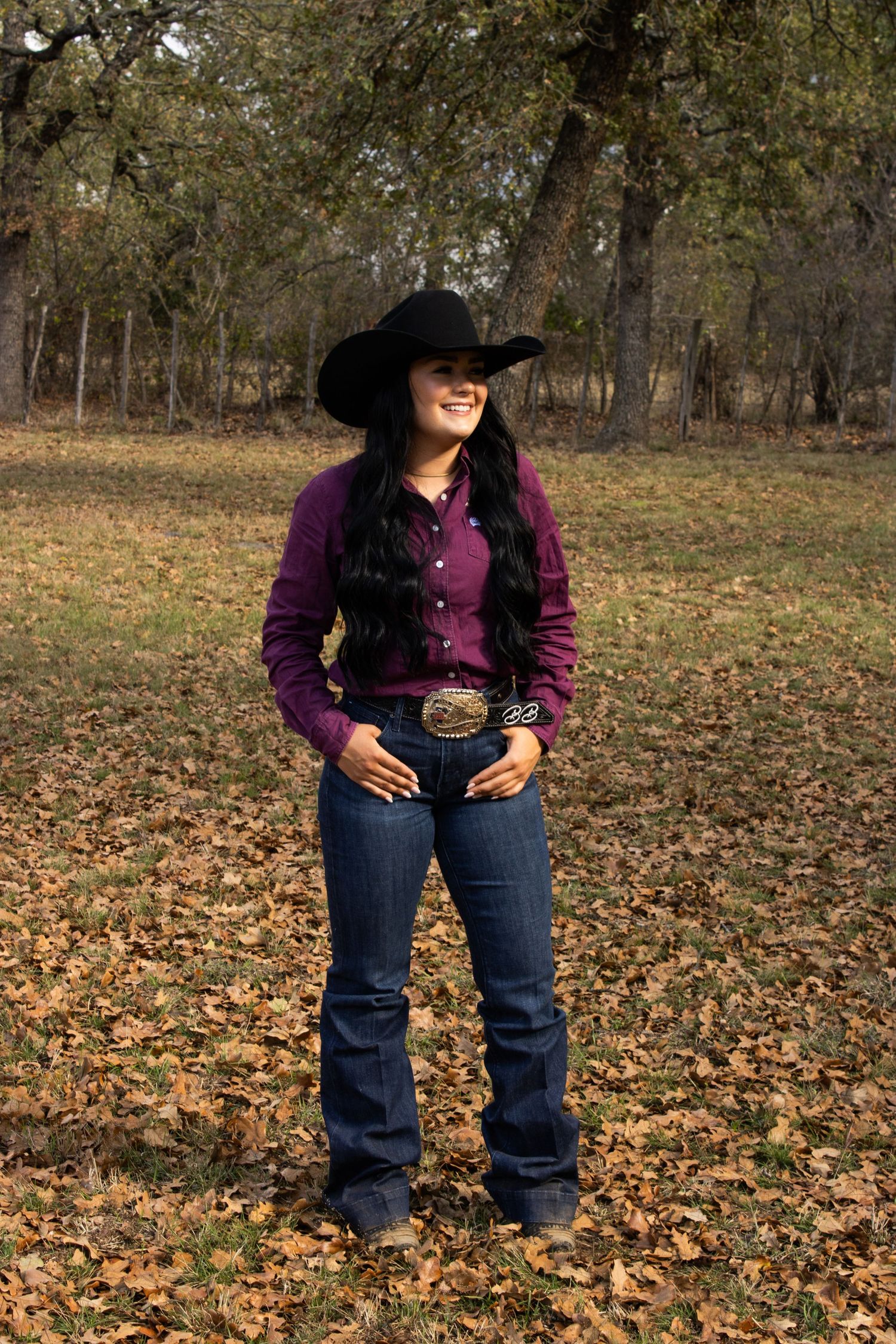Country western style with dark cowboy hat, purple button-down shirt and boot cut jeans in autumn setting.