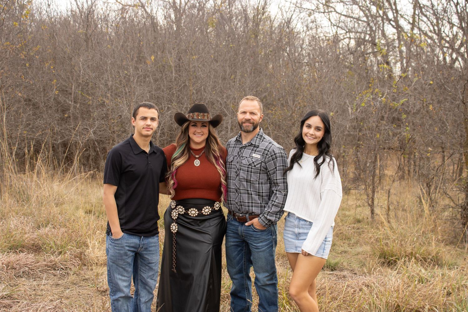 A group of people in casual attire stand together outdoors against a backdrop of bare autumn trees.
