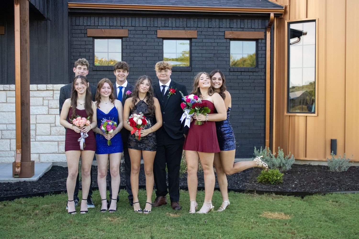 Group photo of formal event attendees lined up against brick building exterior.