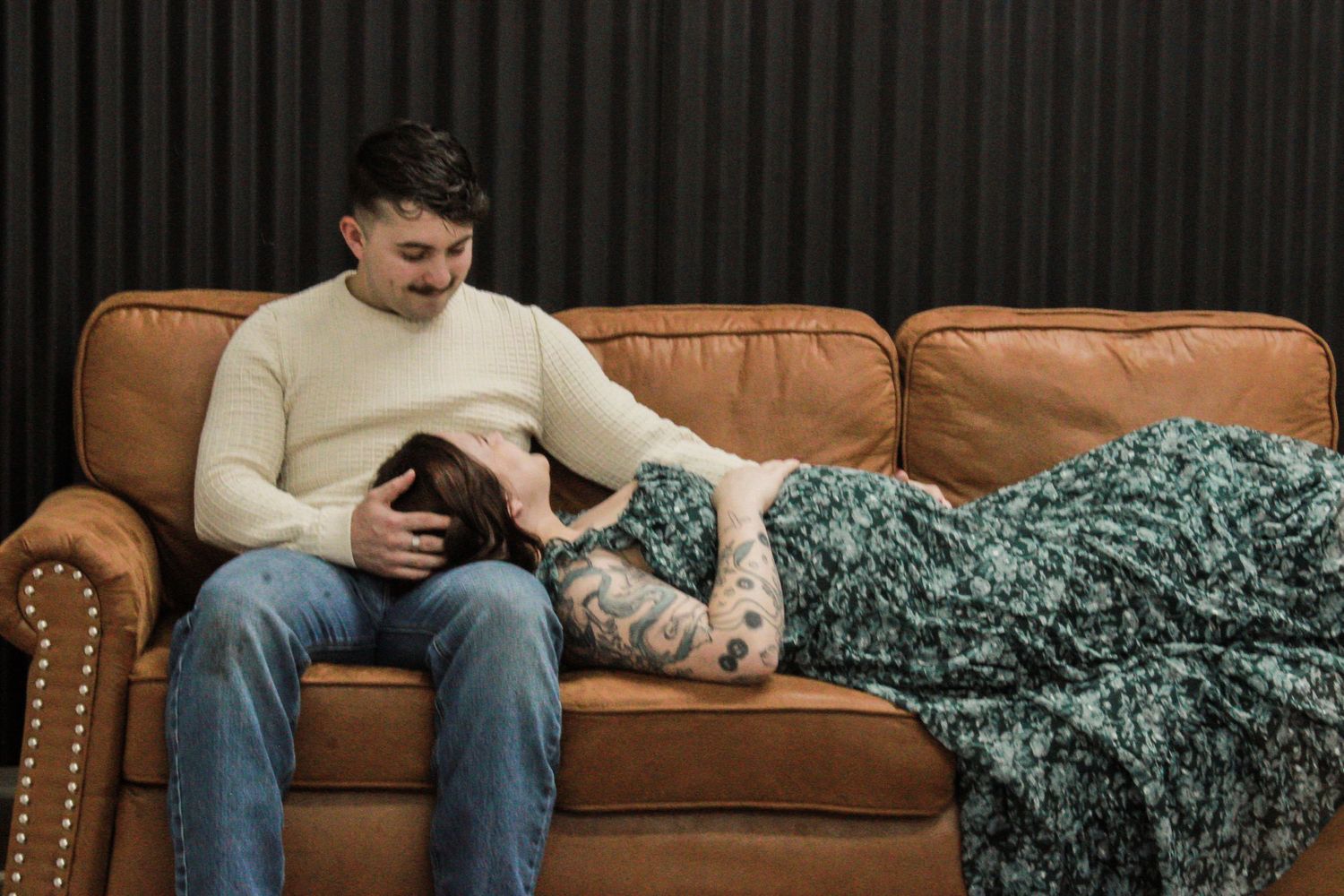 Someone relaxes on a brown leather couch while using a smartphone under a teal throw blanket.