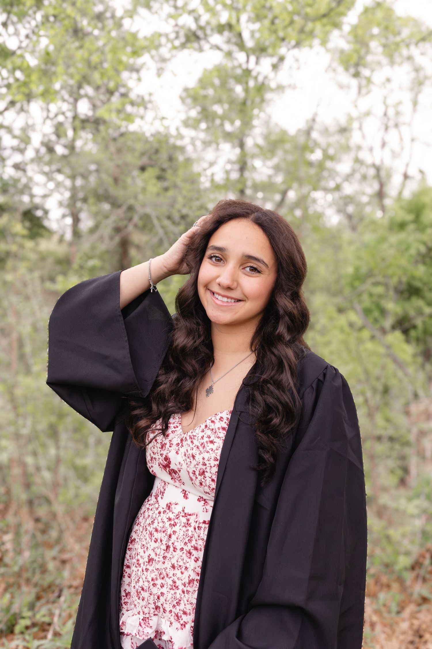 A person in a black blazer and floral dress poses playfully against a natural outdoor background.