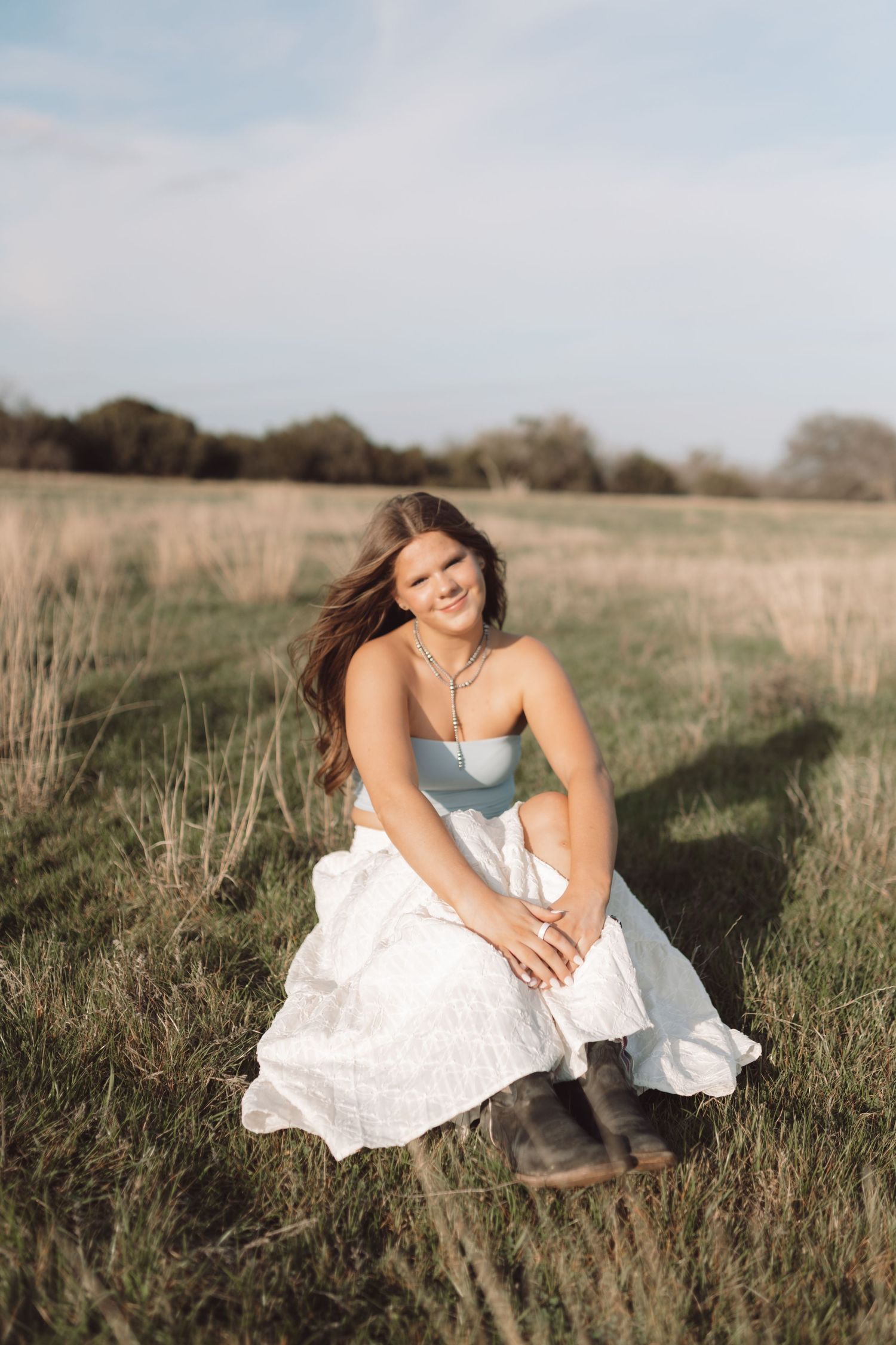 Artistic outdoor photography in tall grass featuring a flowing white dress and pale blue top at golden hour.