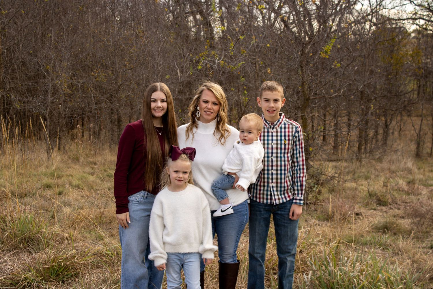 A family poses together outdoors in casual attire during an autumn photoshoot in a natural setting.