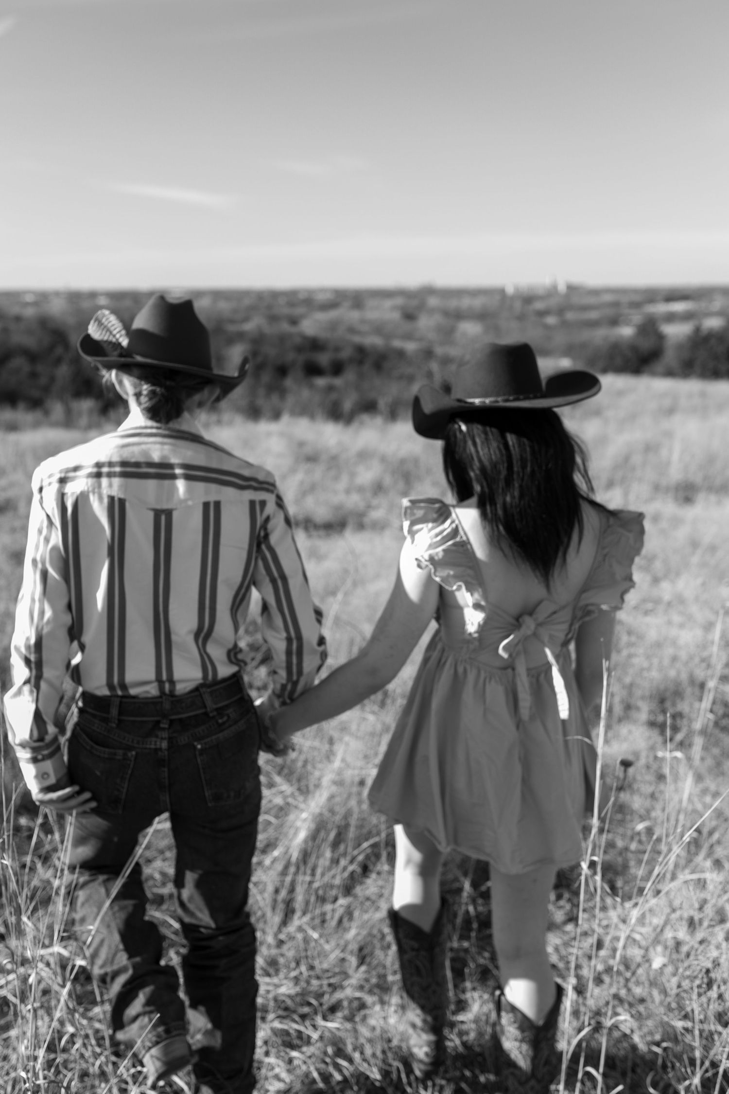Two cowboys in striped shirts walk through a grassy field in black and white photography.