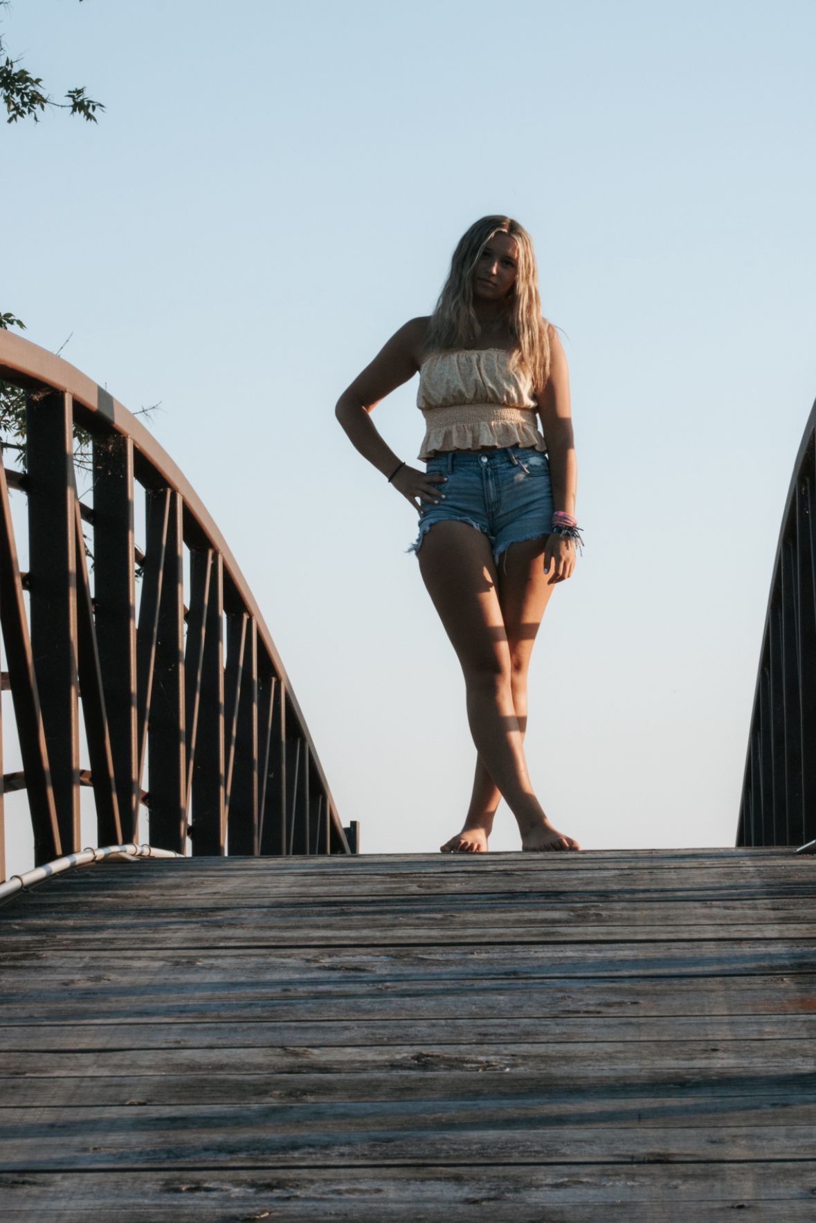 Artistic poses on wooden bridge during summer sunset photoshoot.