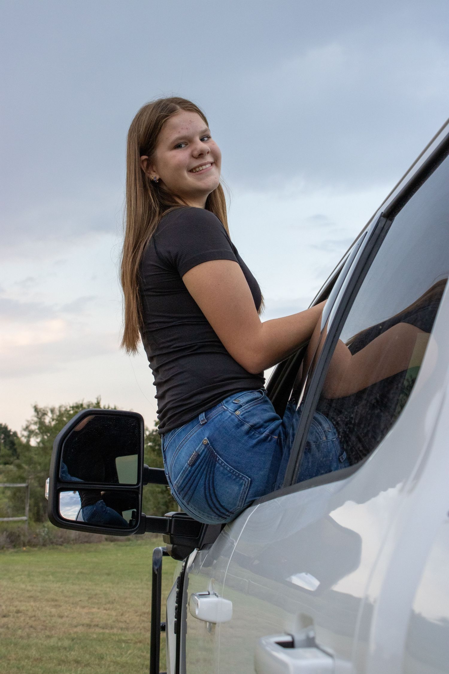 Person climbing into white vehicle at dusk against cloudy sky background.