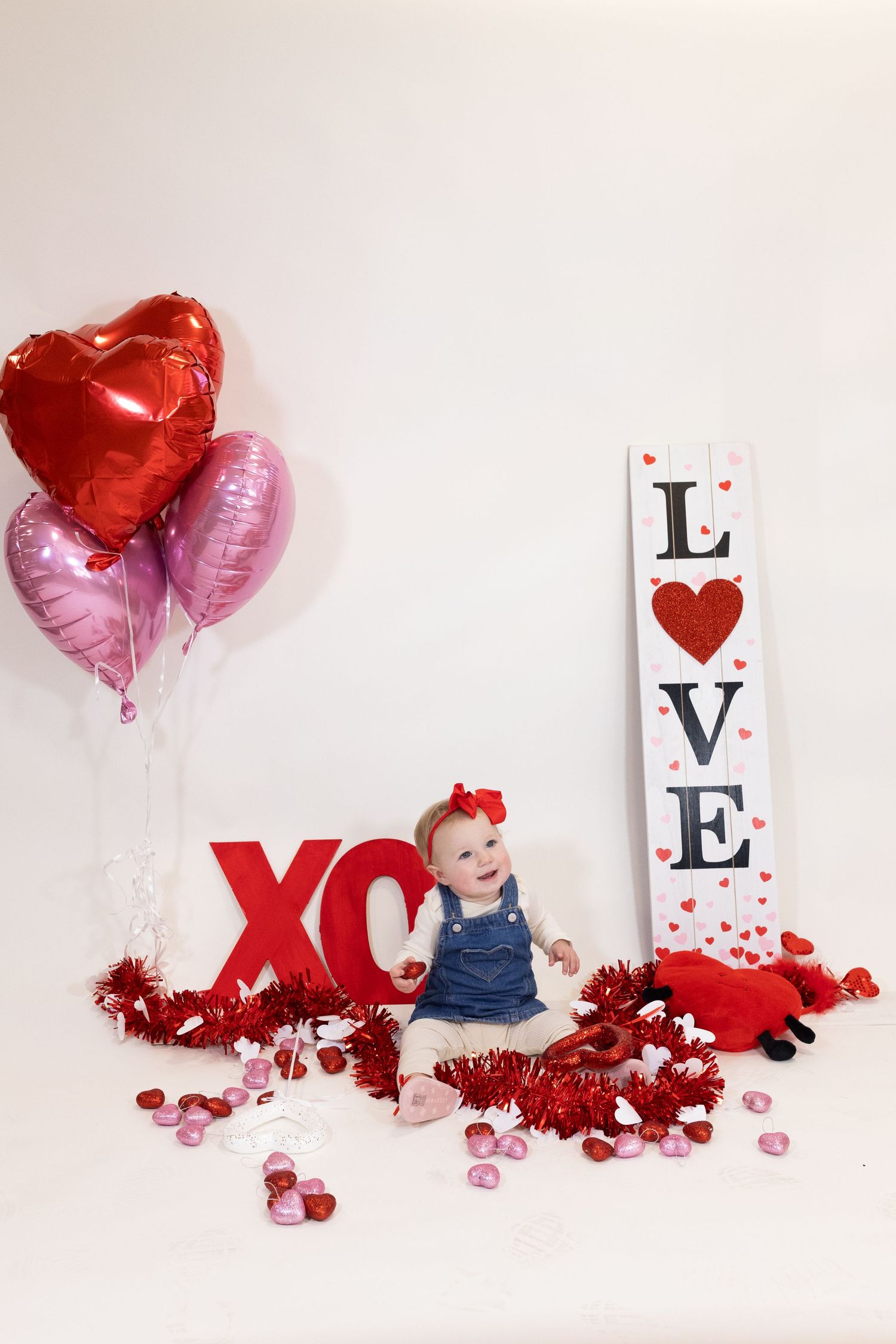 Valentine's day photo setup with red and pink heart balloons, LOVE sign, XO letters and festive decorations on white background.