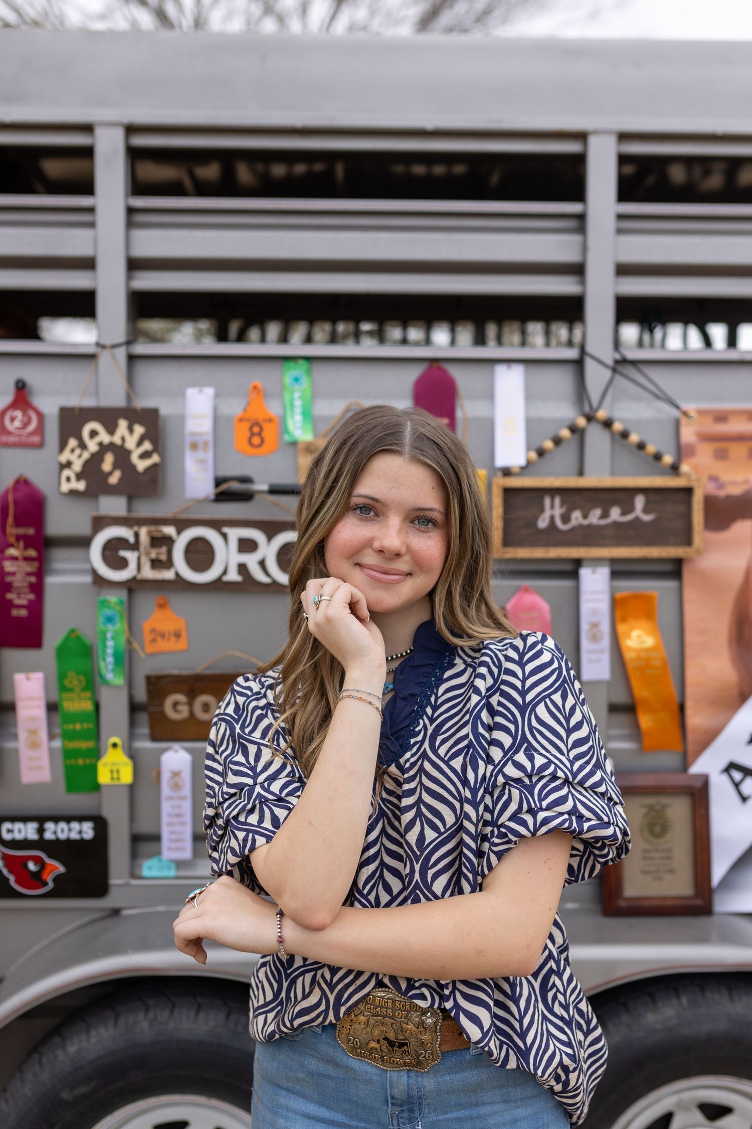 Someone in a blue and white patterned top poses in front of a storefront with a casual, relaxed expression.