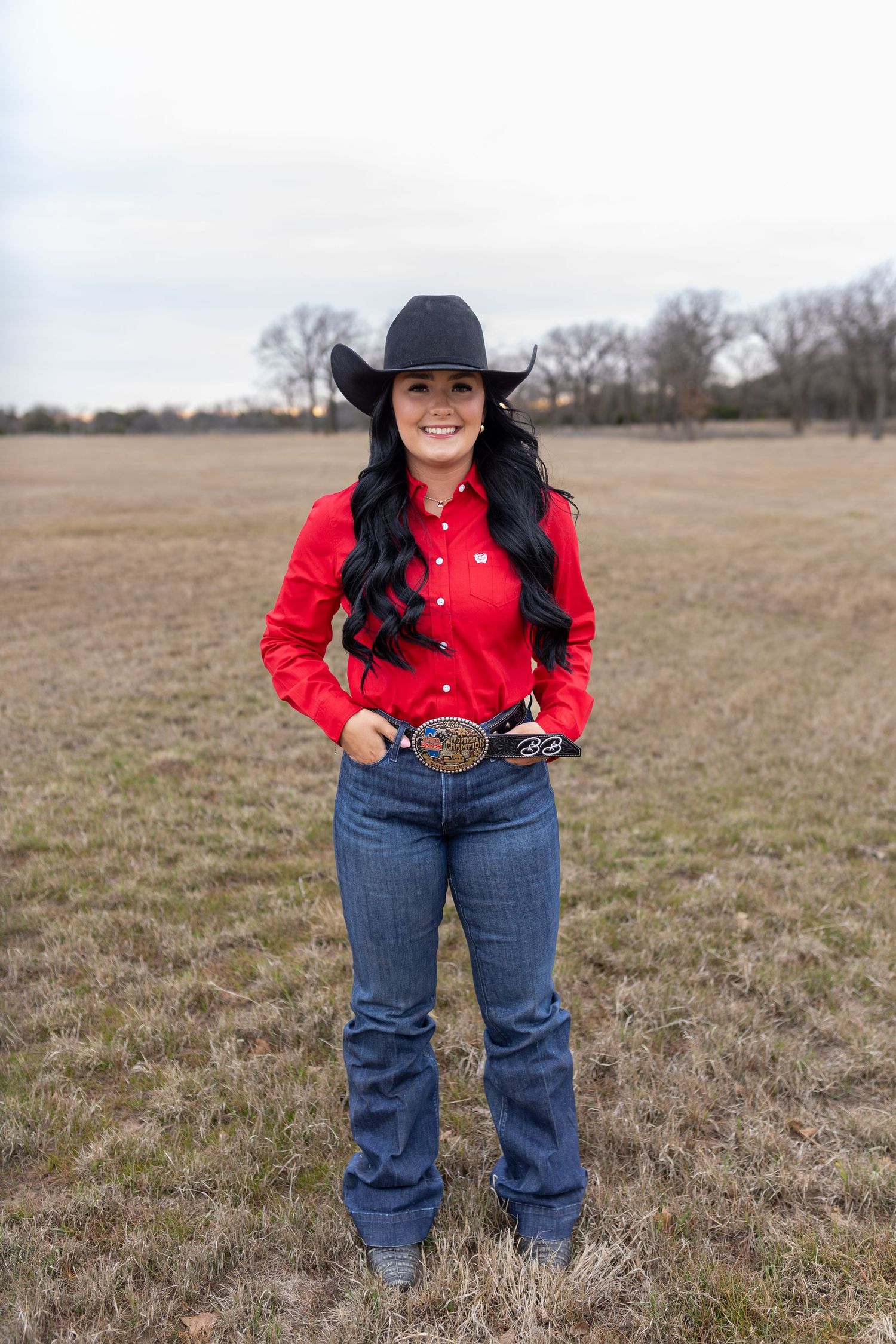 Western style fashion shoot in red shirt, jeans and black hat against winter prairie landscape.