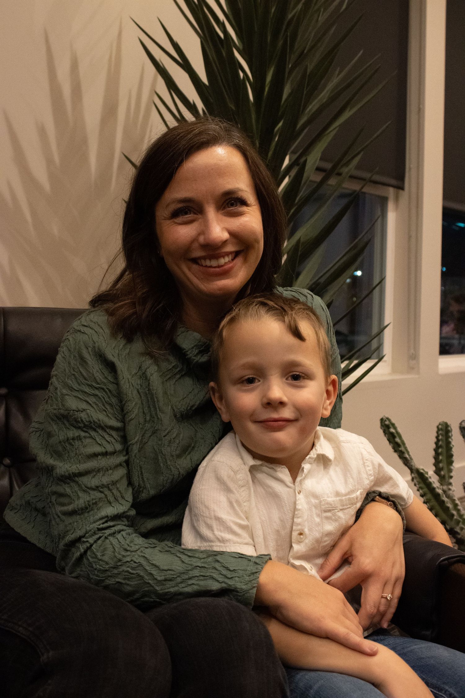 An intimate family portrait in a living room setting with a large palm plant in the background.