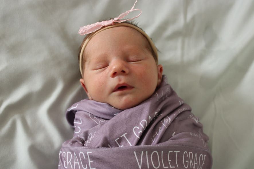 Sleeping newborn baby wearing pink headband on white bedding.