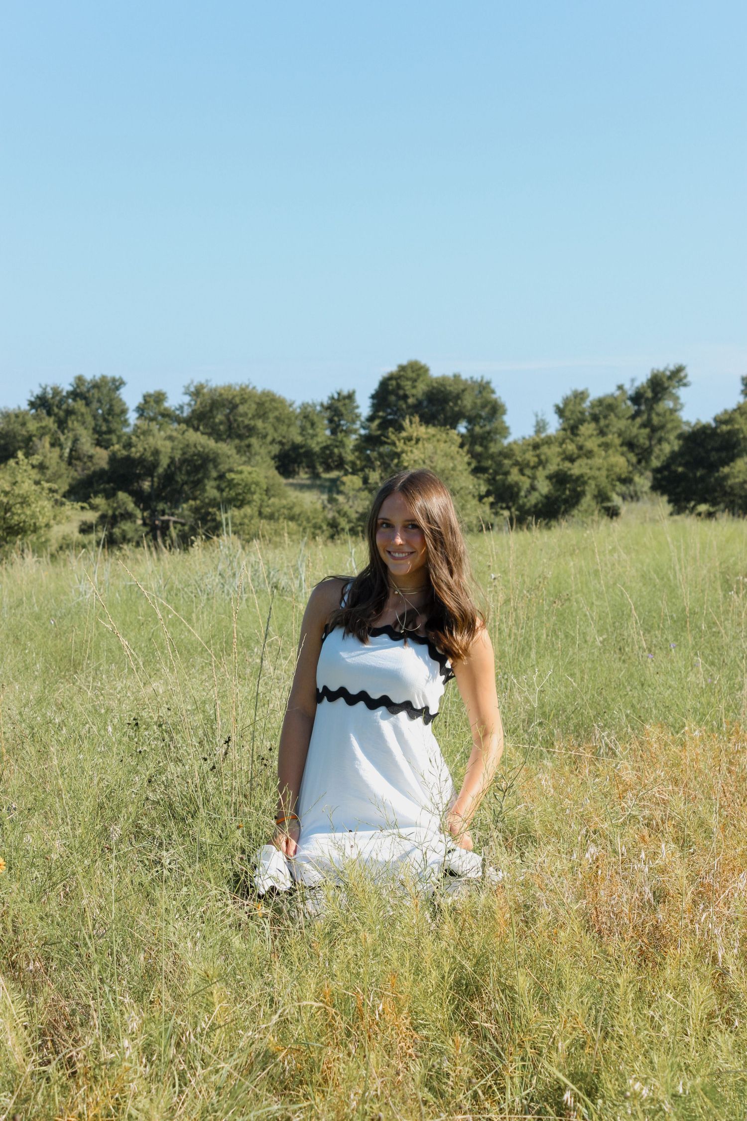 Person in white dress standing in sunny meadow with tall grass.