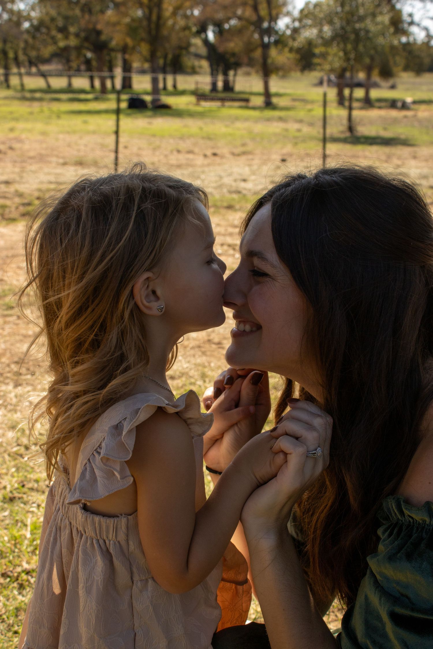 A sweet candid moment between two people sharing laughter in a sunlit outdoor setting with trees in the background.