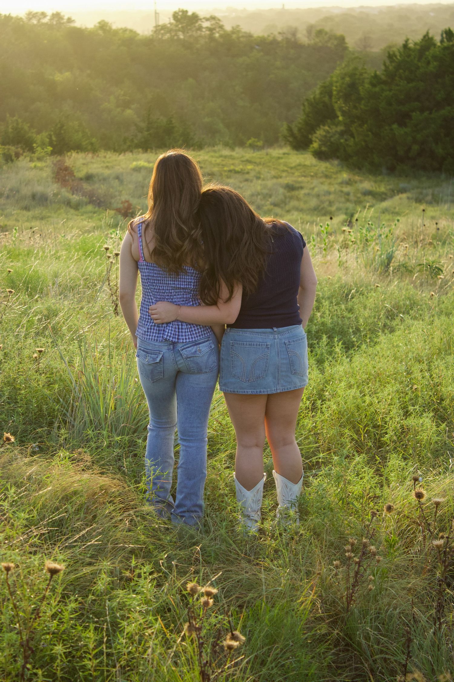 Two people walking through a lush green field at sunset.
