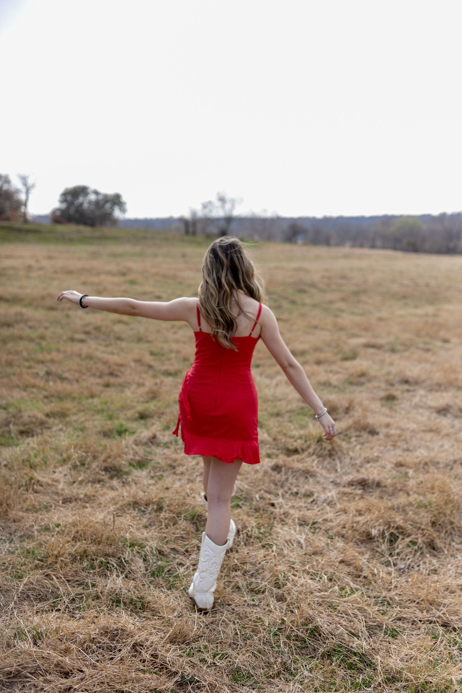 Person in red dress and white socks dances freely in an open field during golden hour.