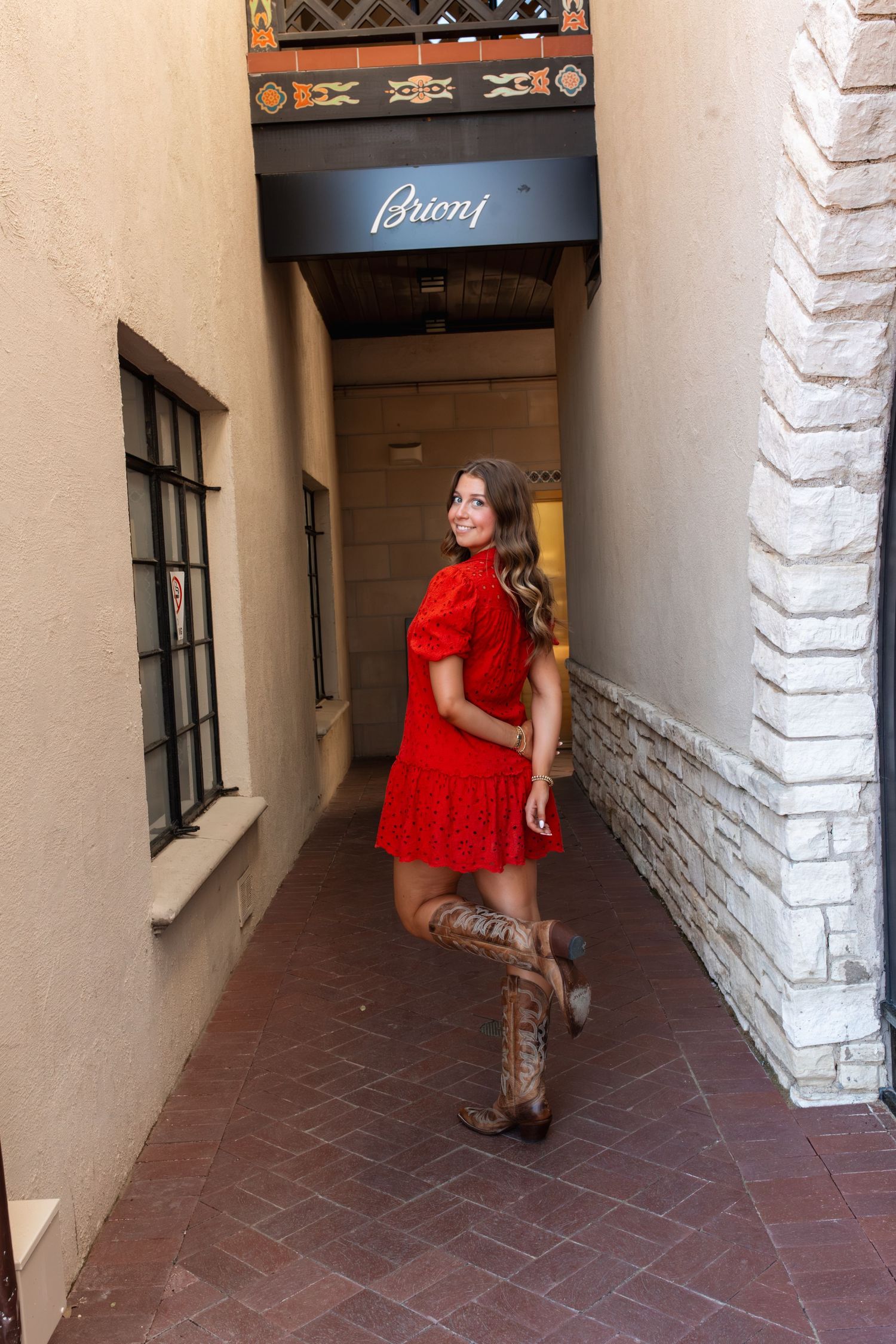 Person in red dress posing against white stucco wall and tiled floor in covered walkway.