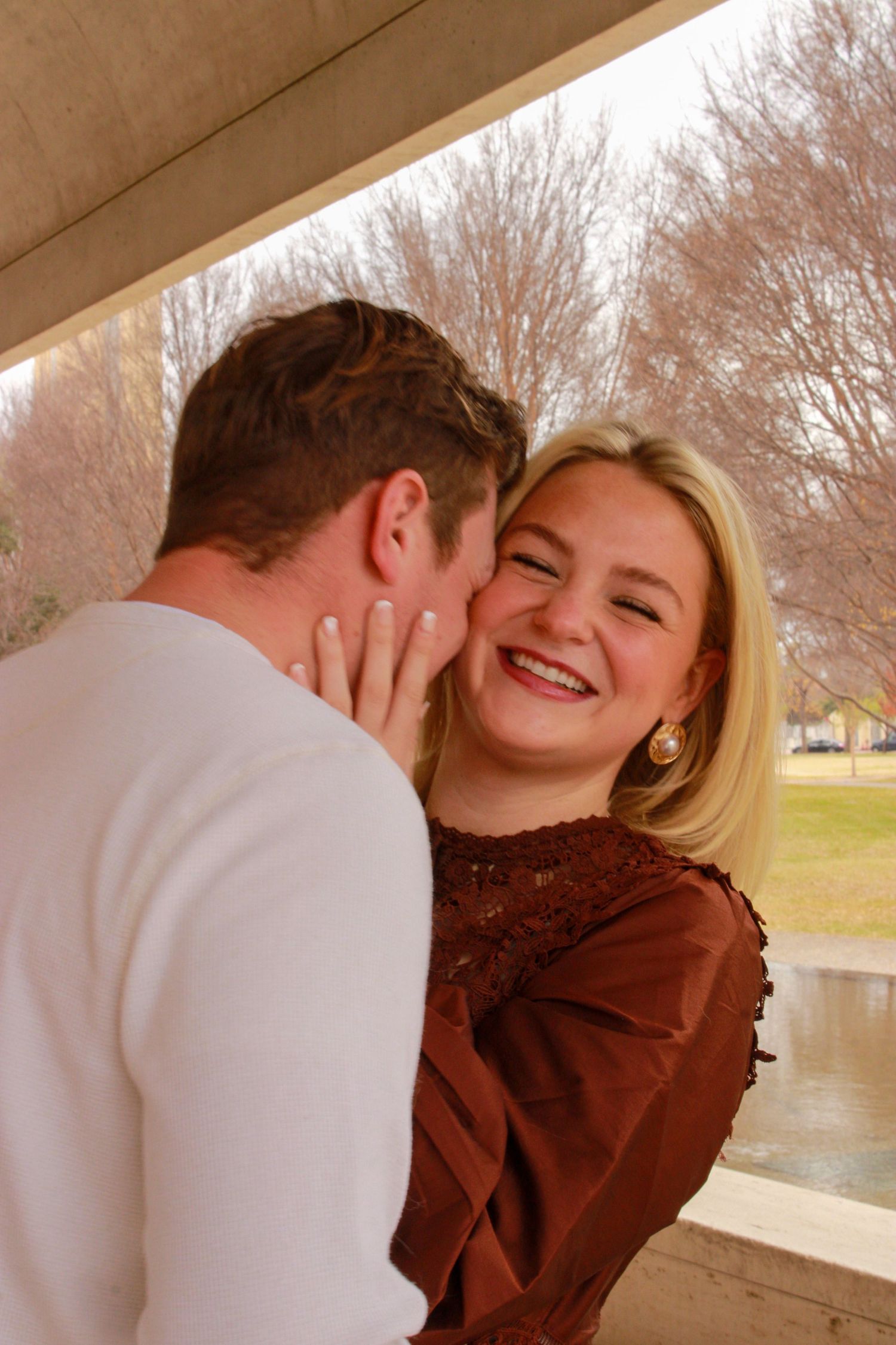 A couple embraces and shares a joyful moment together near a lake on an autumn day.