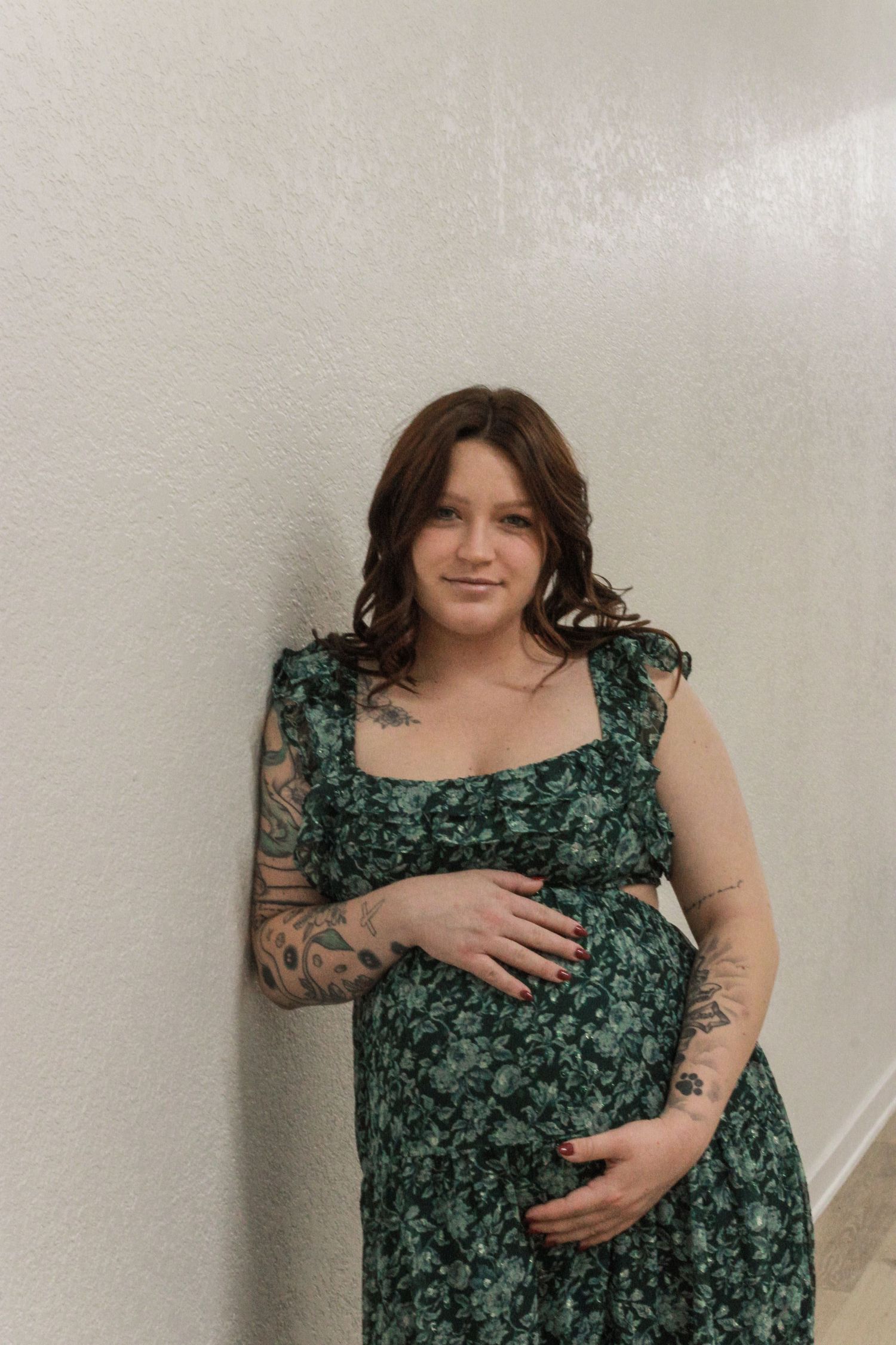 A person wearing a green floral dress poses against a light colored wall in a series of four connected photos.