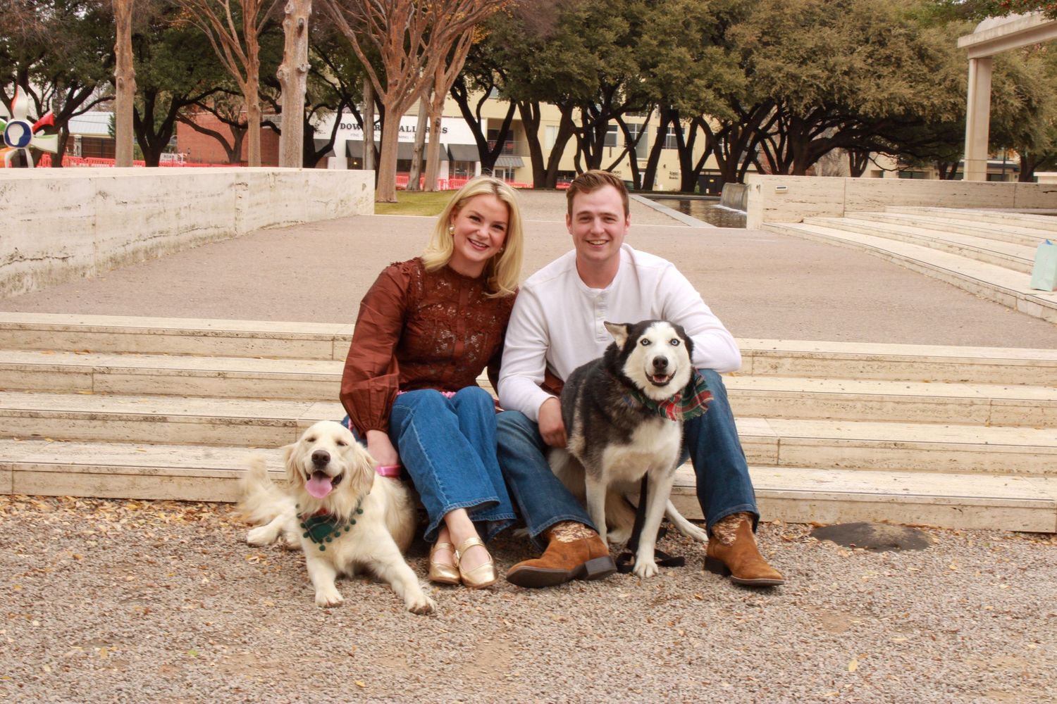 Couple sits on outdoor steps with their white dog during an engagement photo session at sunset.