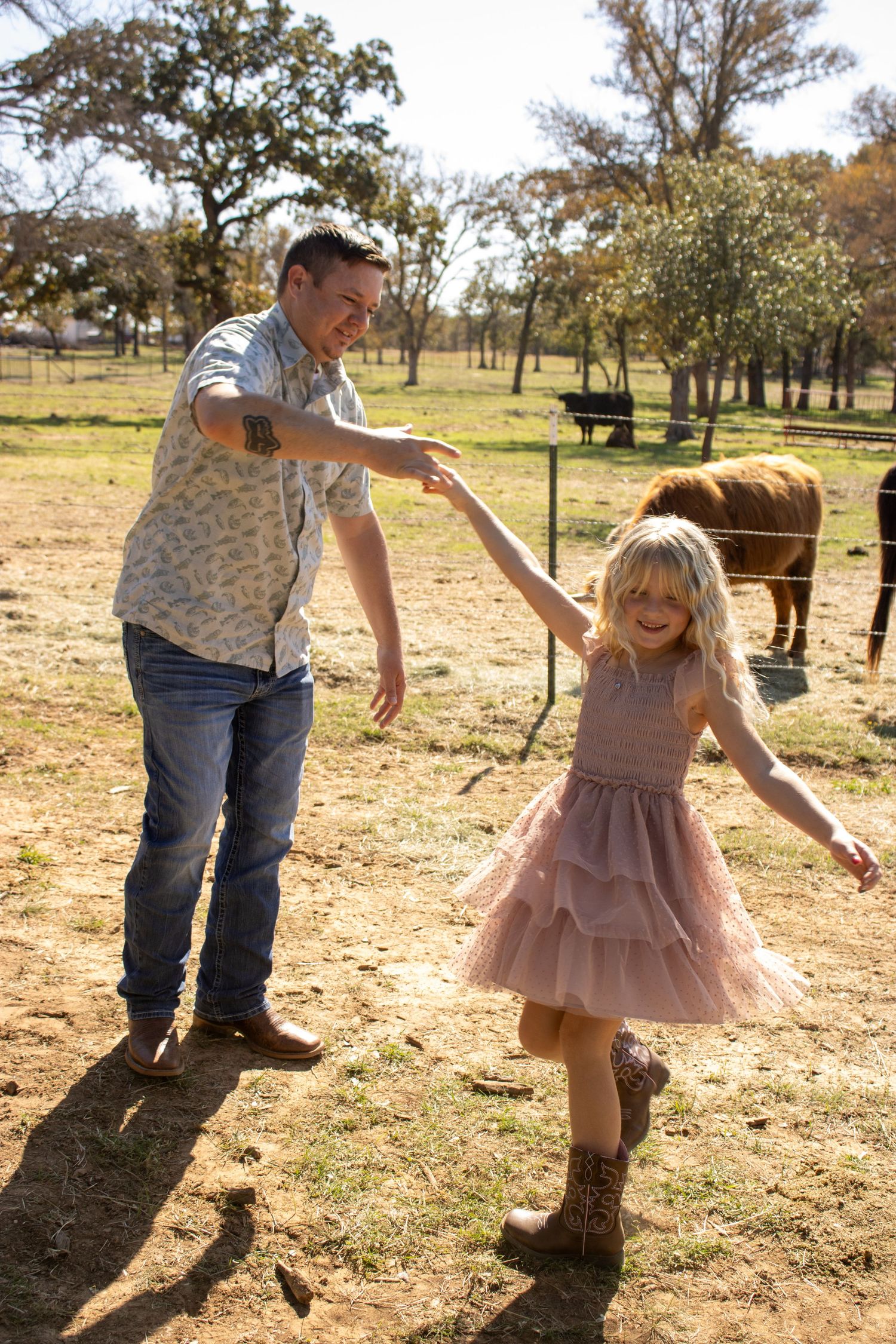 Dancing together on a sunny day at a ranch with horses grazing in the background.