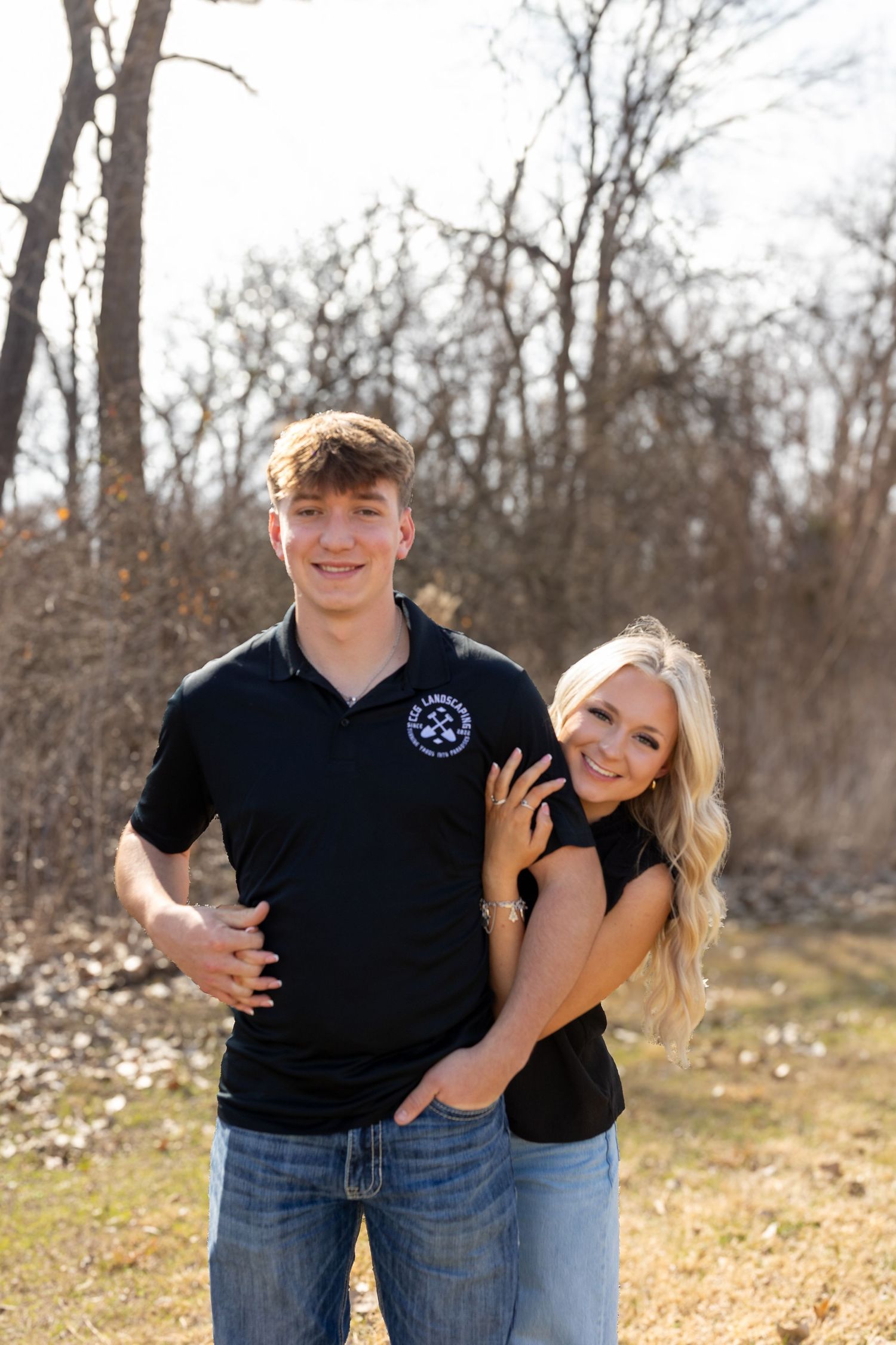 A couple poses outdoors in matching black shirts on a sunny day.
