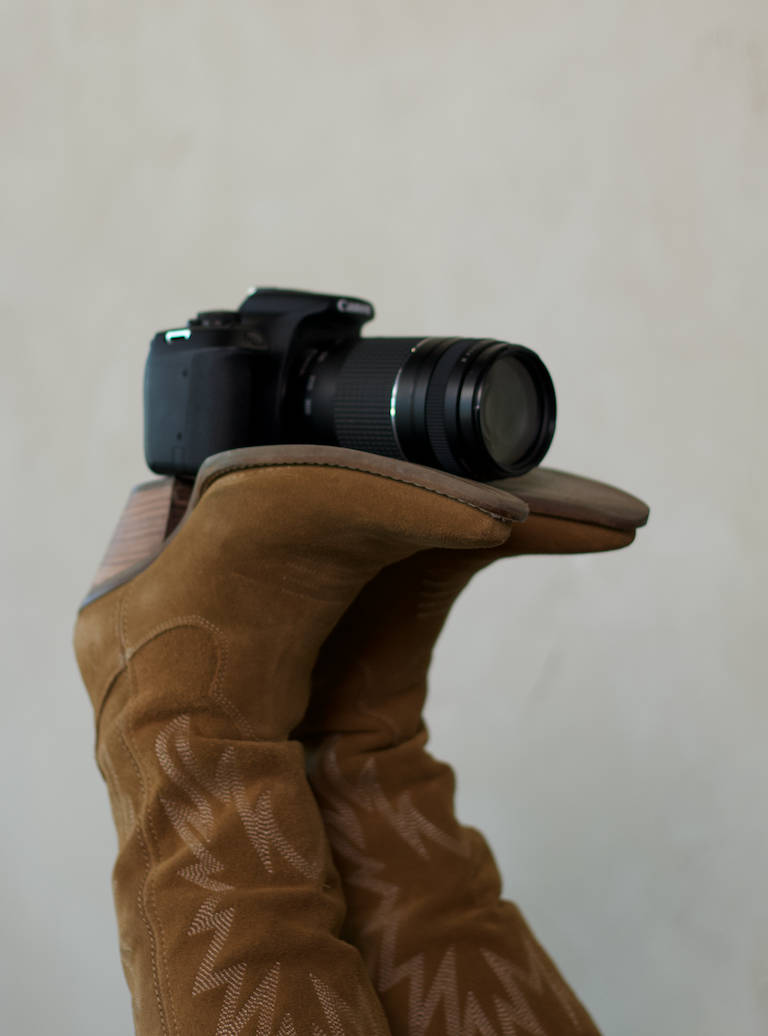 A brown suede boot with a camera lens peeking out from behind, showing a creative photography perspective.