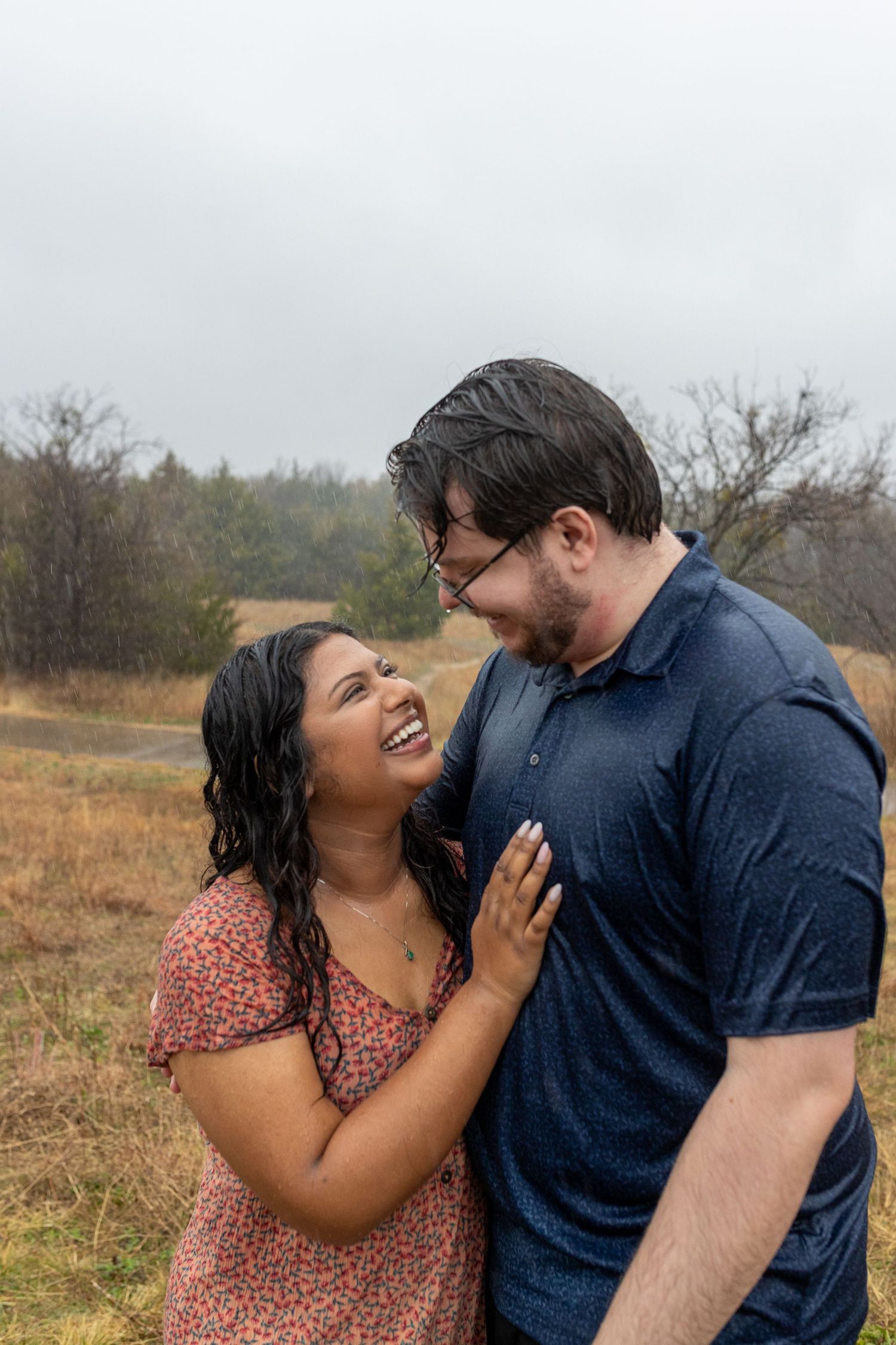 A couple shares a joyful laugh together while standing in a misty field on an overcast day.