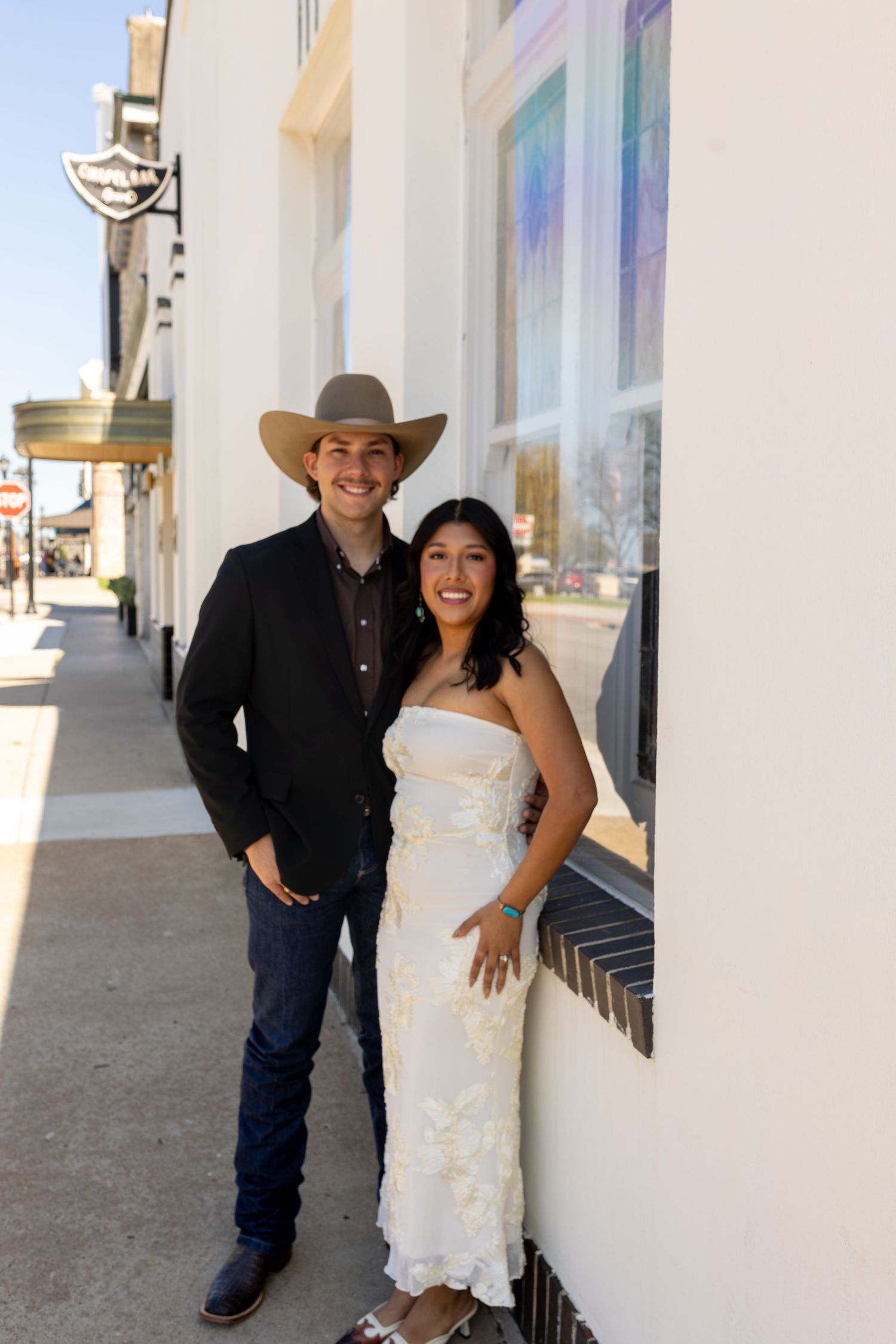 A couple poses together in western attire against a white building wall in a series of casual outdoor shots.
