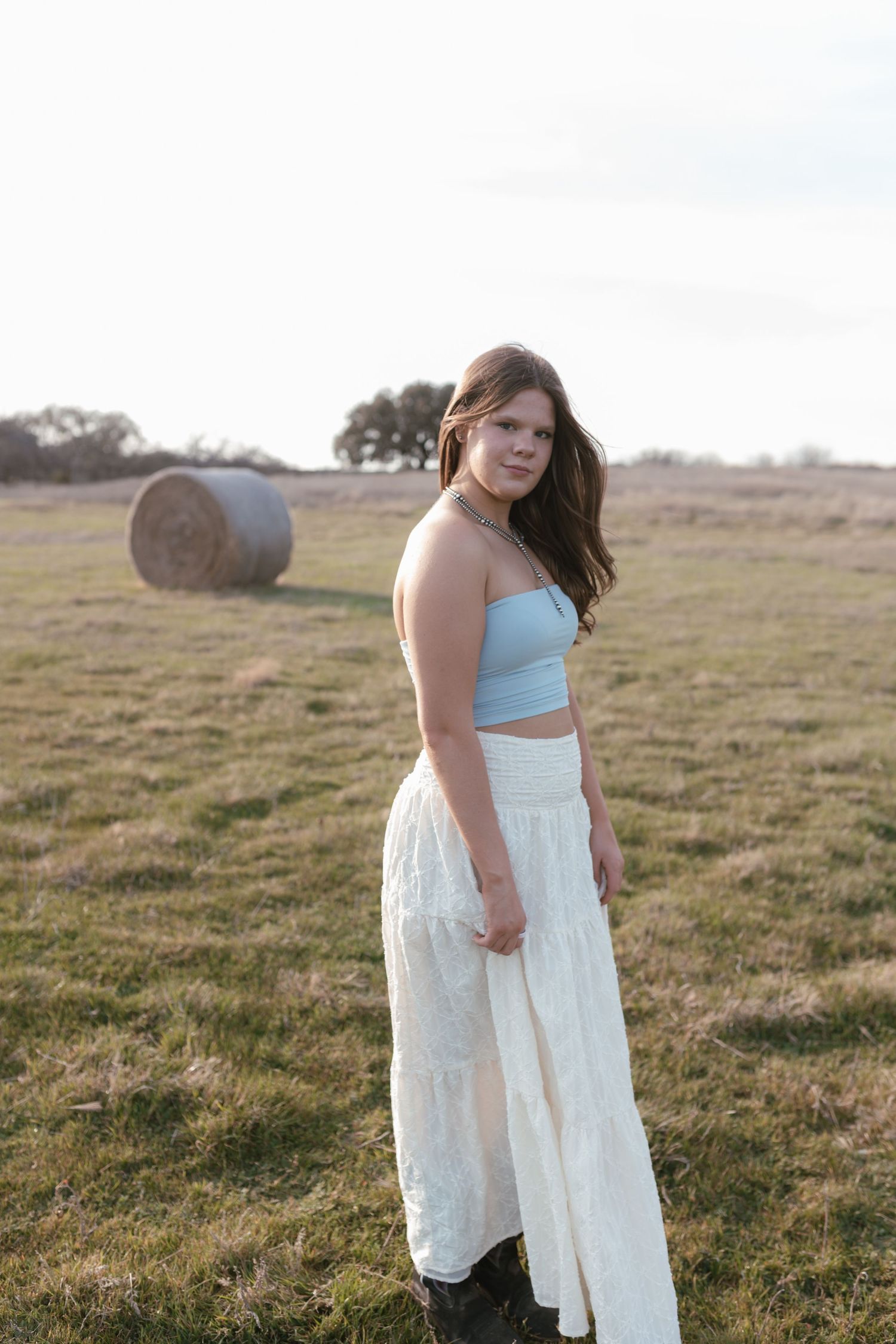Dreamy pastoral photoshoot in an open field with round hay bales visible in the background.