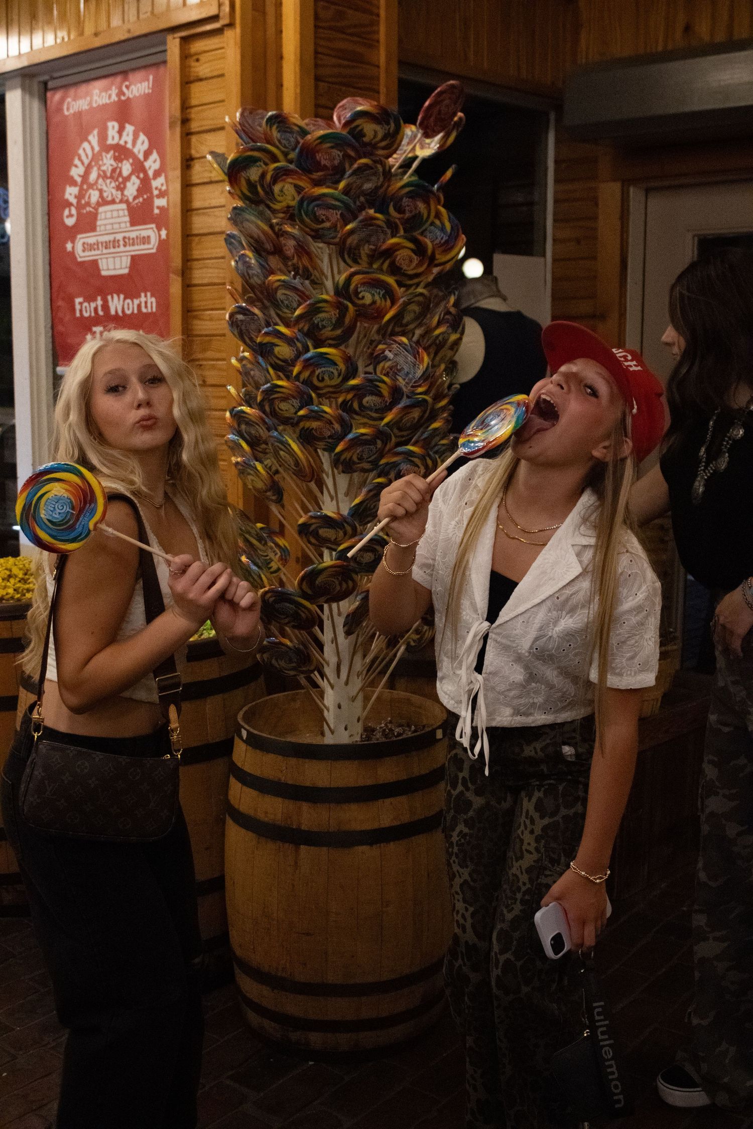 Friends posing with lollipops near wooden barrel display.