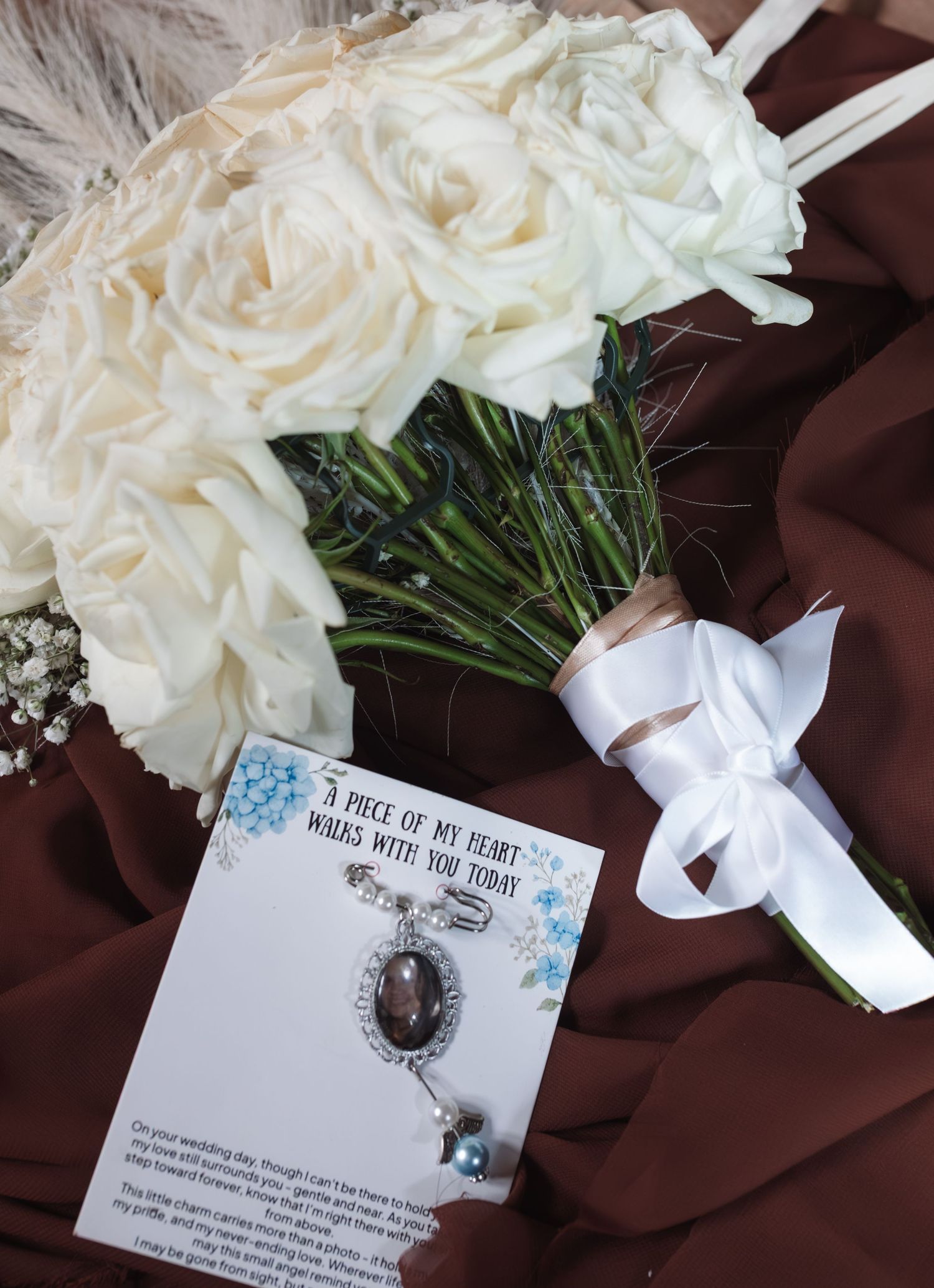 White rose bridal bouquet with satin ribbon beside a memorial charm card reading A Piece of My Heart Walks With You Today.
