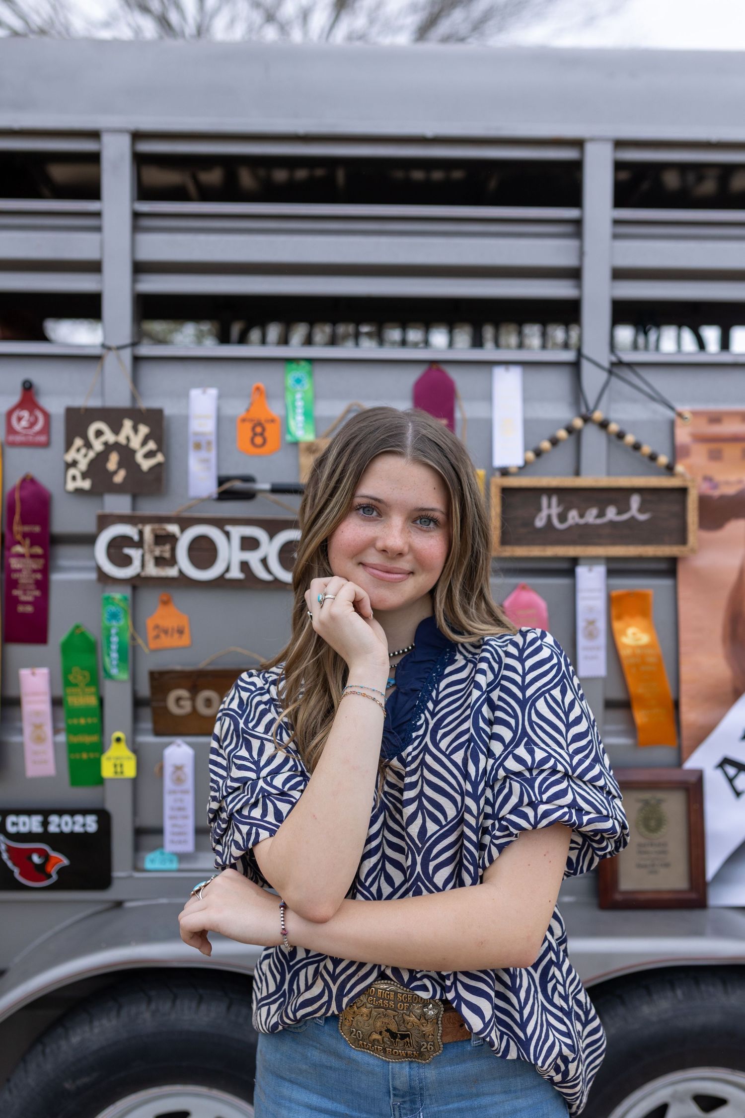 A person in a blue and white patterned dress poses near a storefront with a car visible in the background.