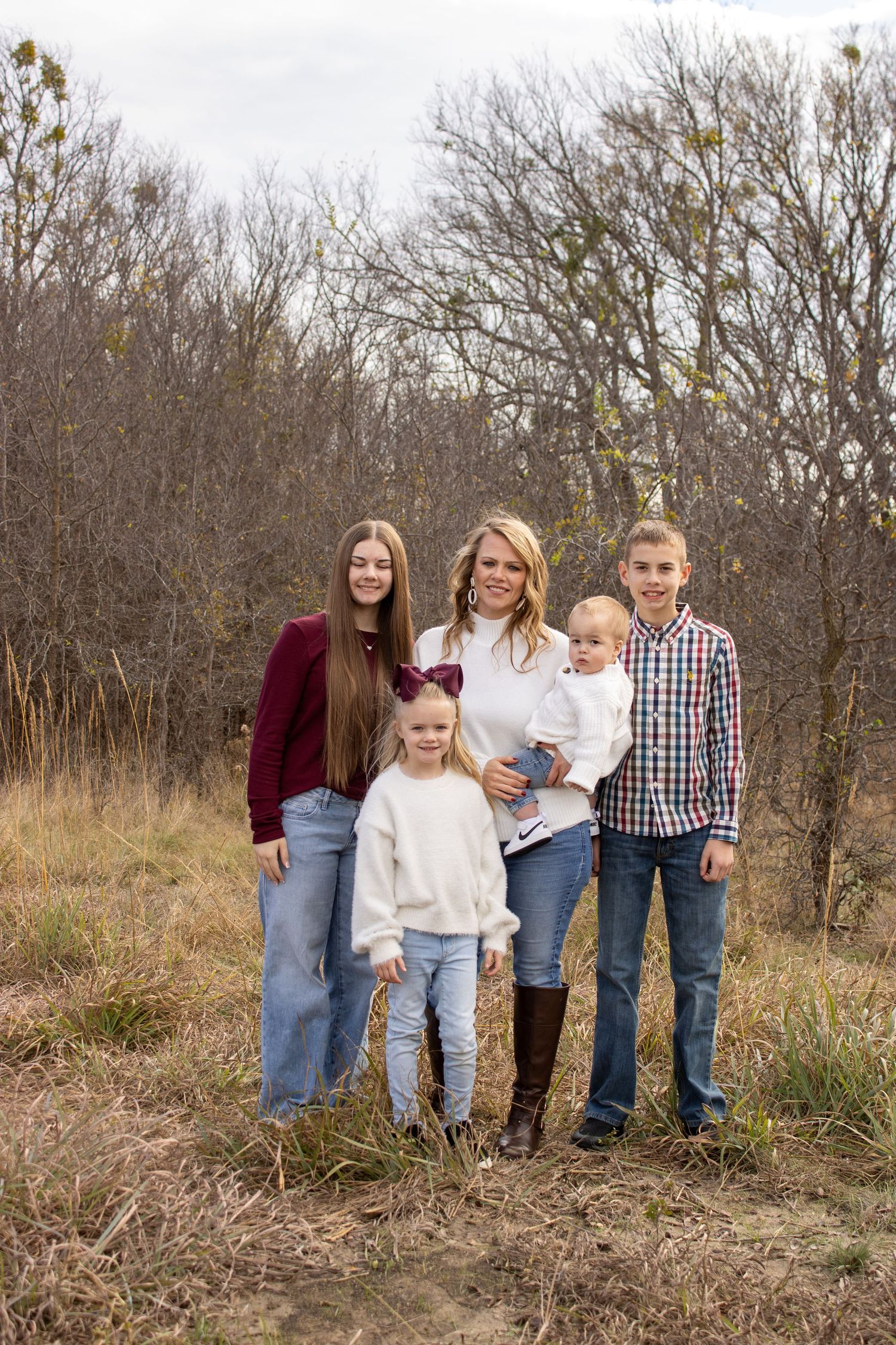 A group stands together outdoors for a casual portrait against a backdrop of bare trees and autumn grass.