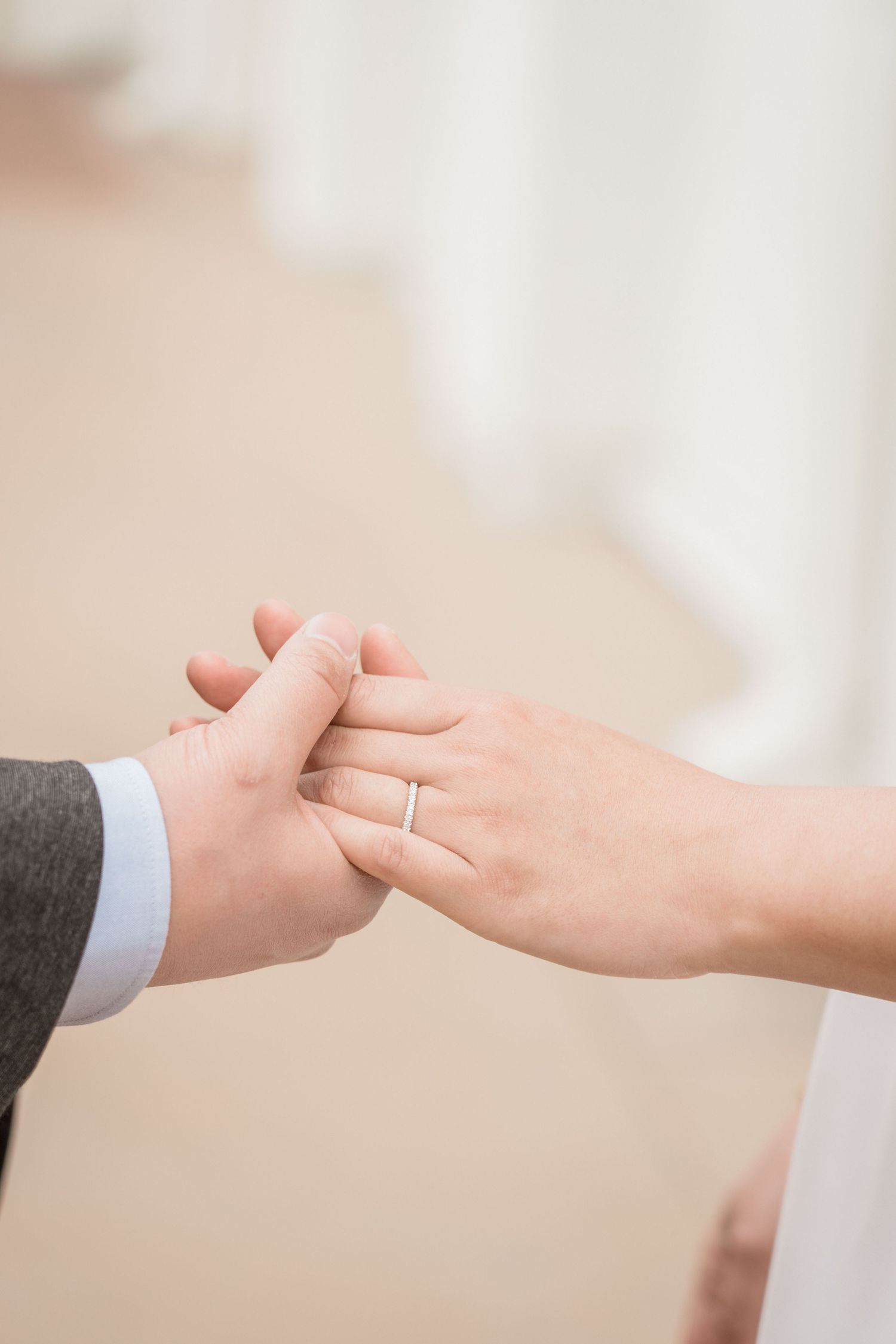 Close-up of newlyweds holding hands with elegant wedding band on bride's finger.