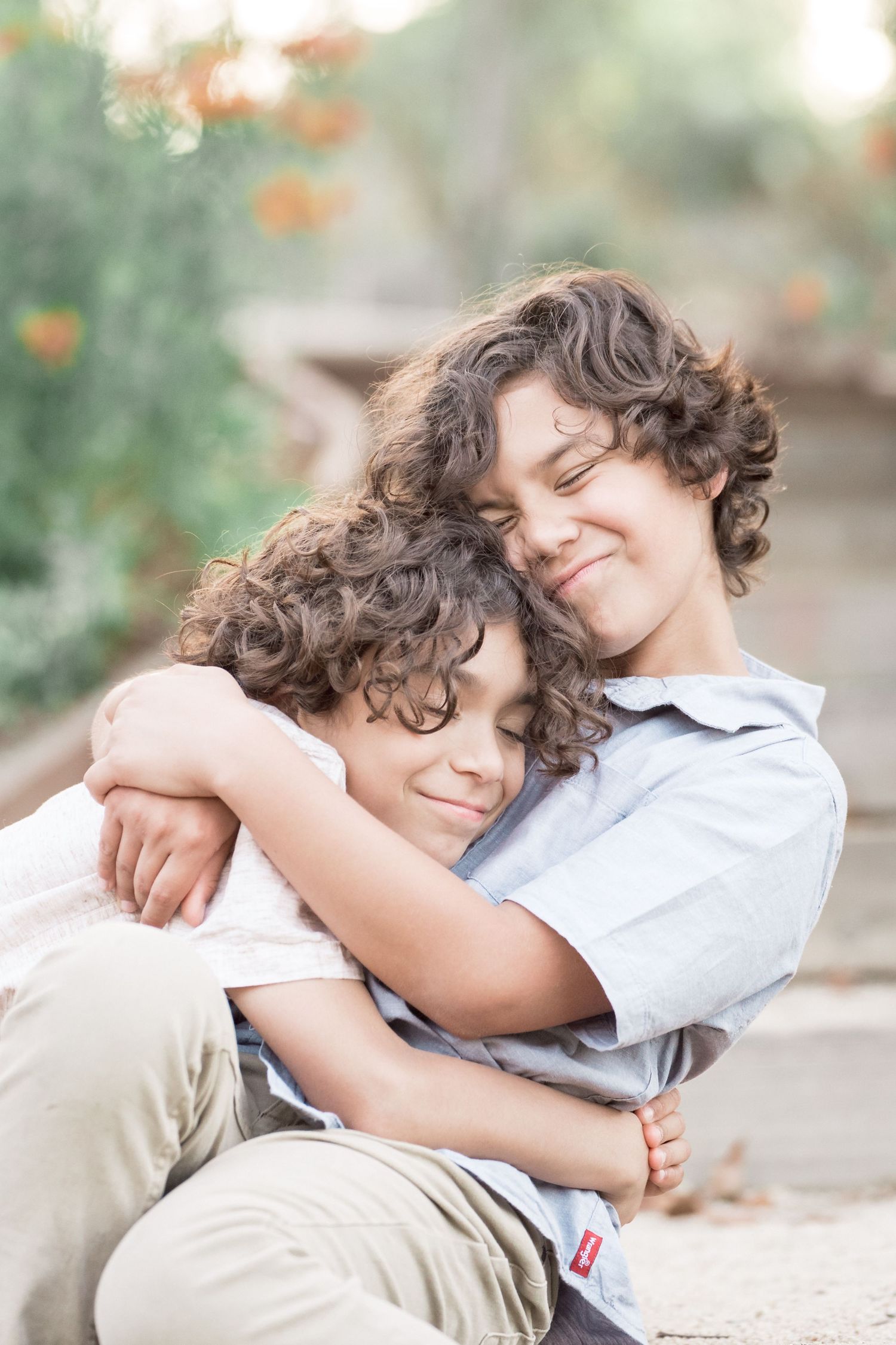 Two curly-haired brothers sharing a warm embrace while sitting outdoors in natural light.
