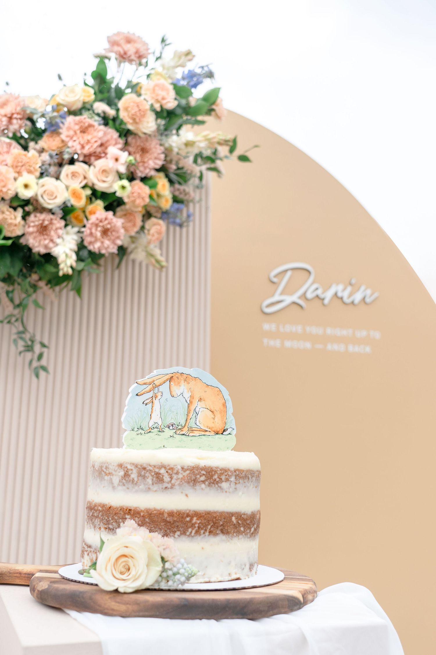 Two-tier naked cake with bunny topper and floral backdrop for baby named Darin.