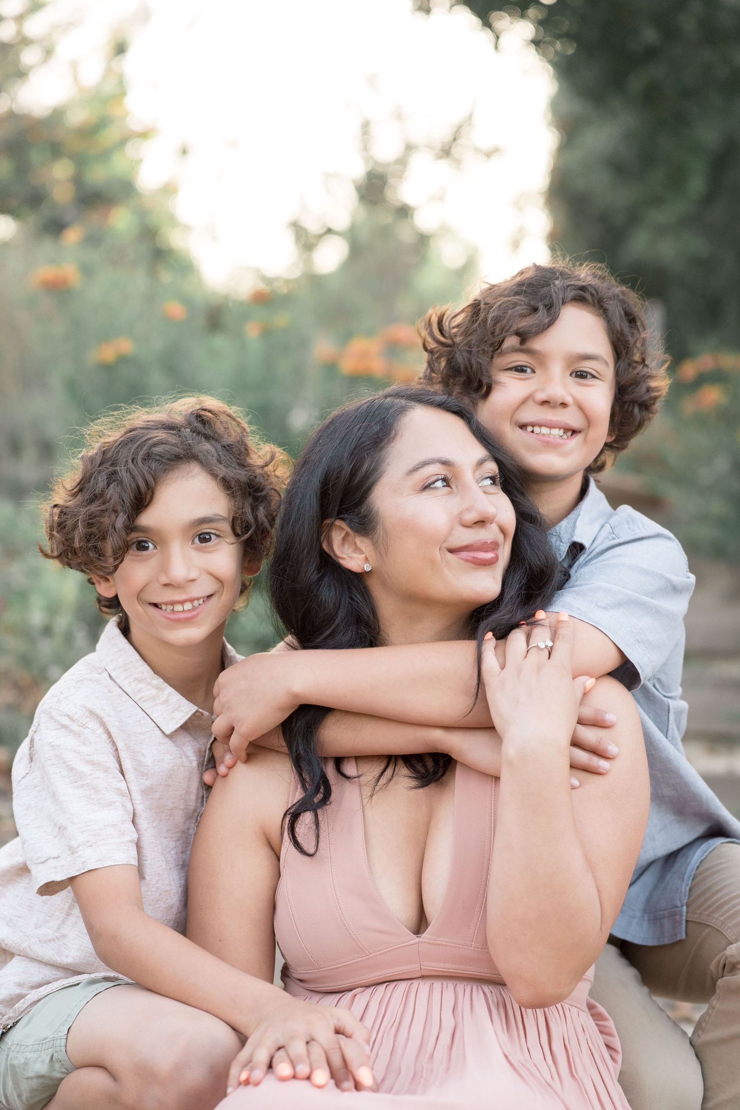 Smiling Hispanic mother in pink dress with her two curly-haired sons outdoors.