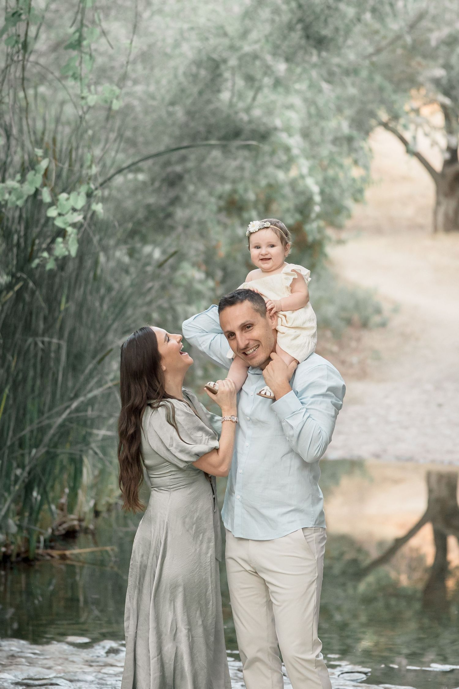 Happy family with father holding baby girl on shoulders near a peaceful garden pond.