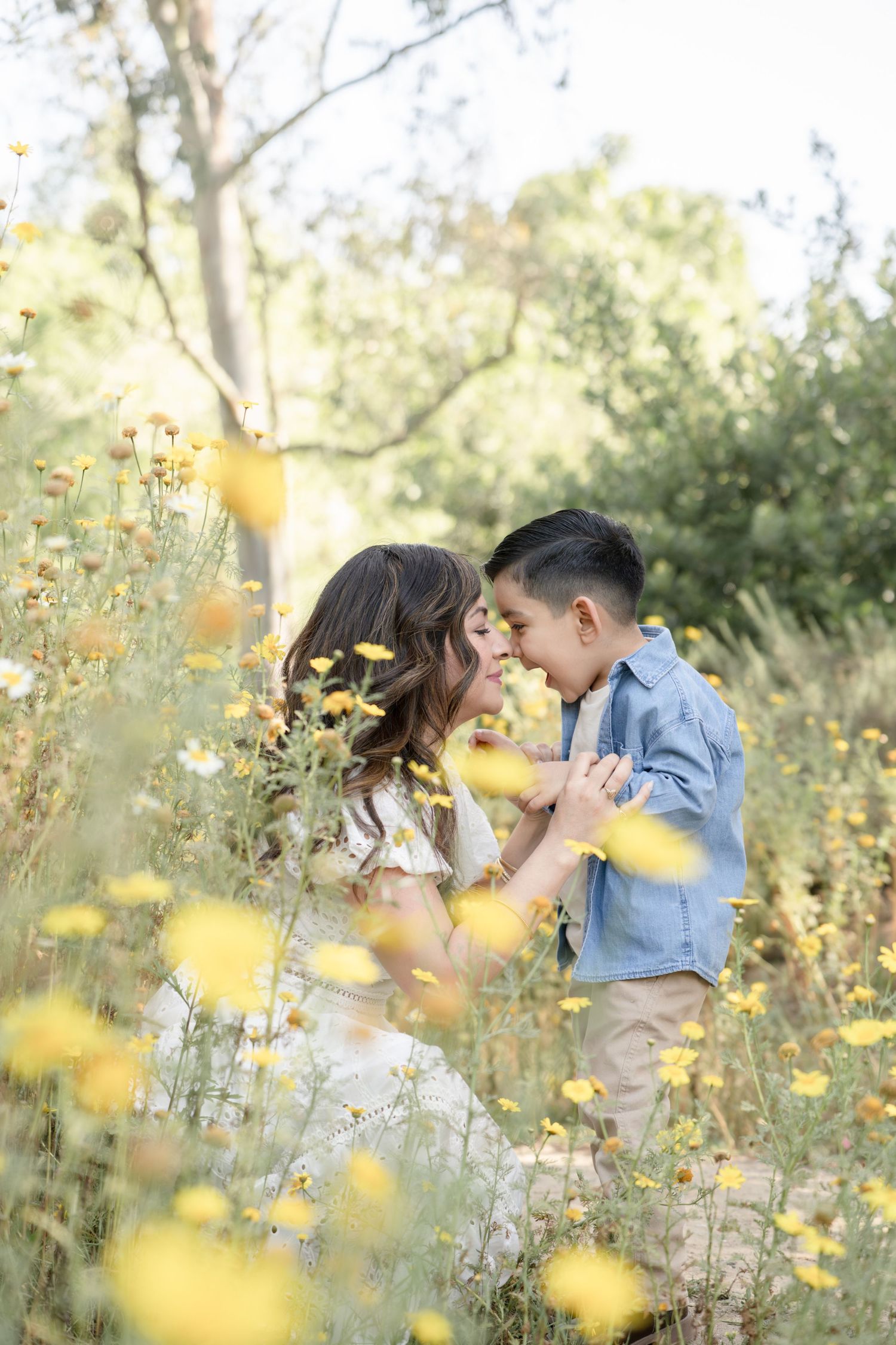 Mother and young son touch foreheads tenderly in a field of yellow wildflowers.