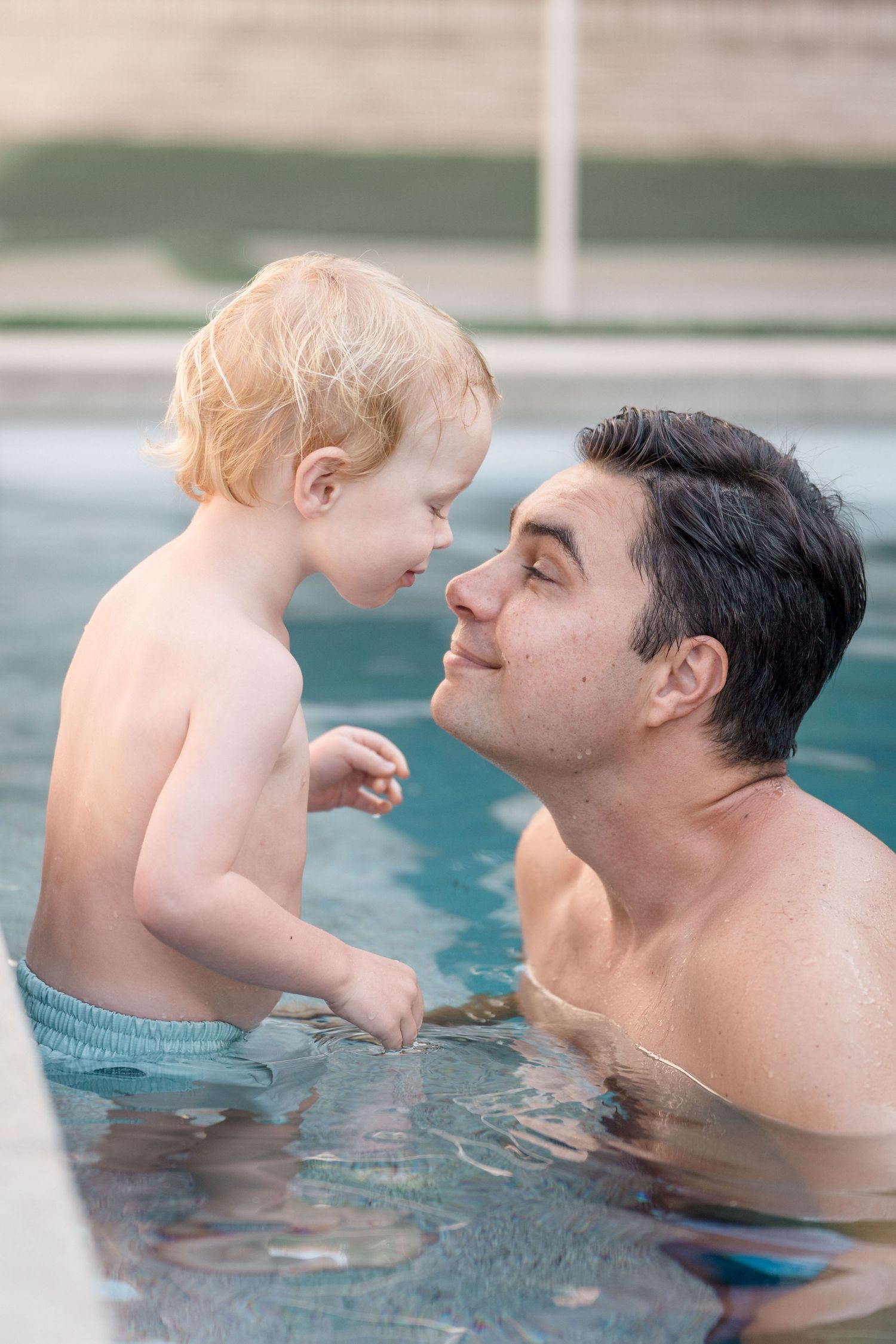 Father and blonde toddler sharing a tender moment in a swimming pool.