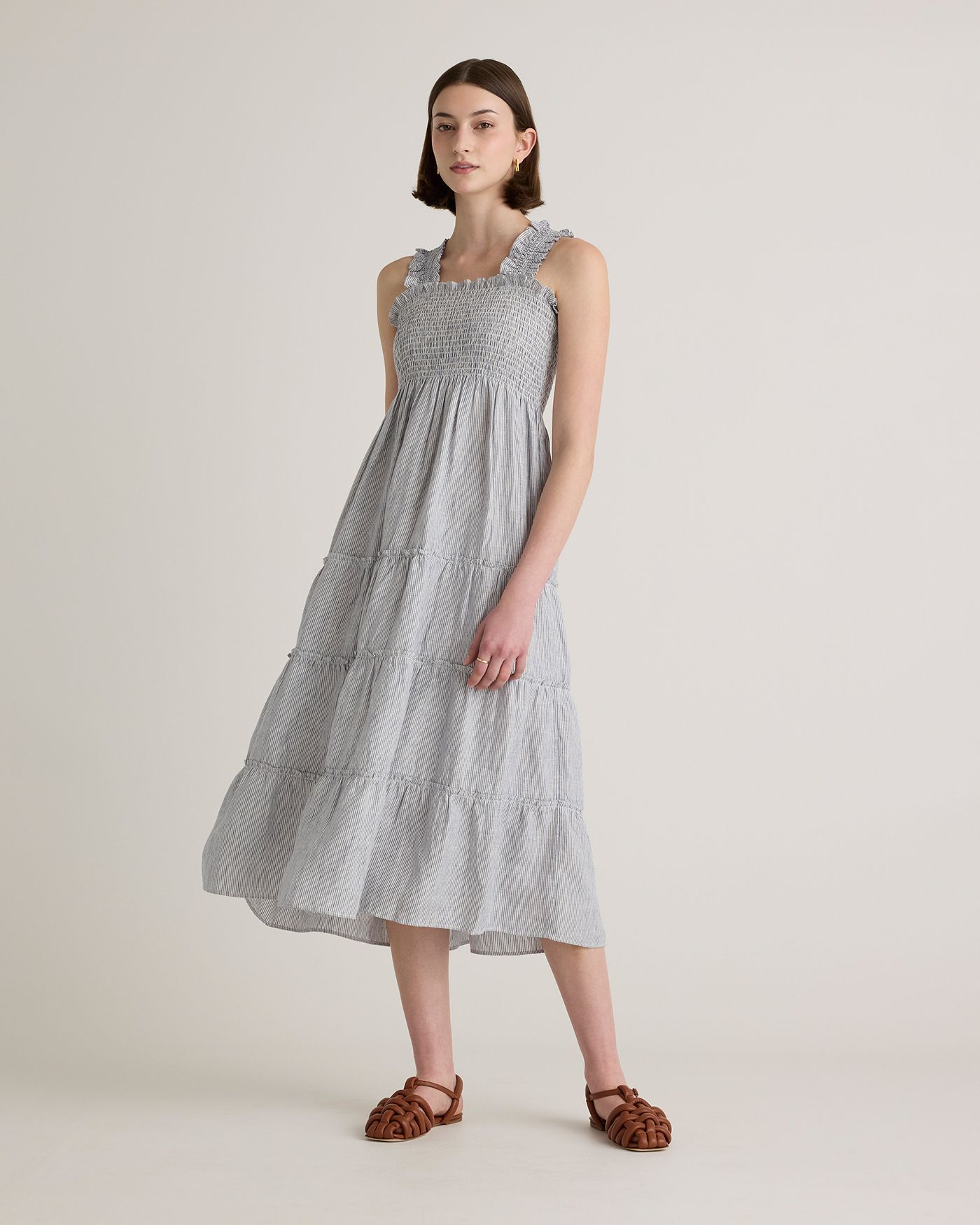 A woman models a sleeveless tiered midi dress with a smocked bodice in a blue and white stripe pattern.