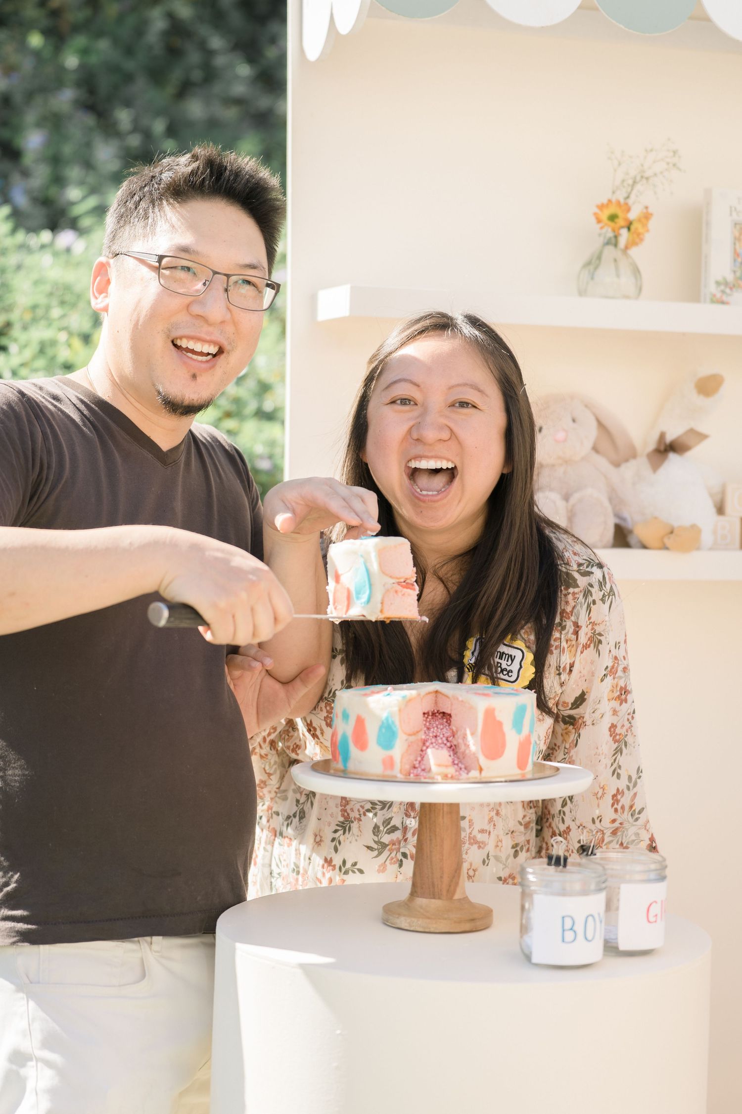 Excited Asian couple cutting open a gender reveal cake showing pink inside at a baby shower.