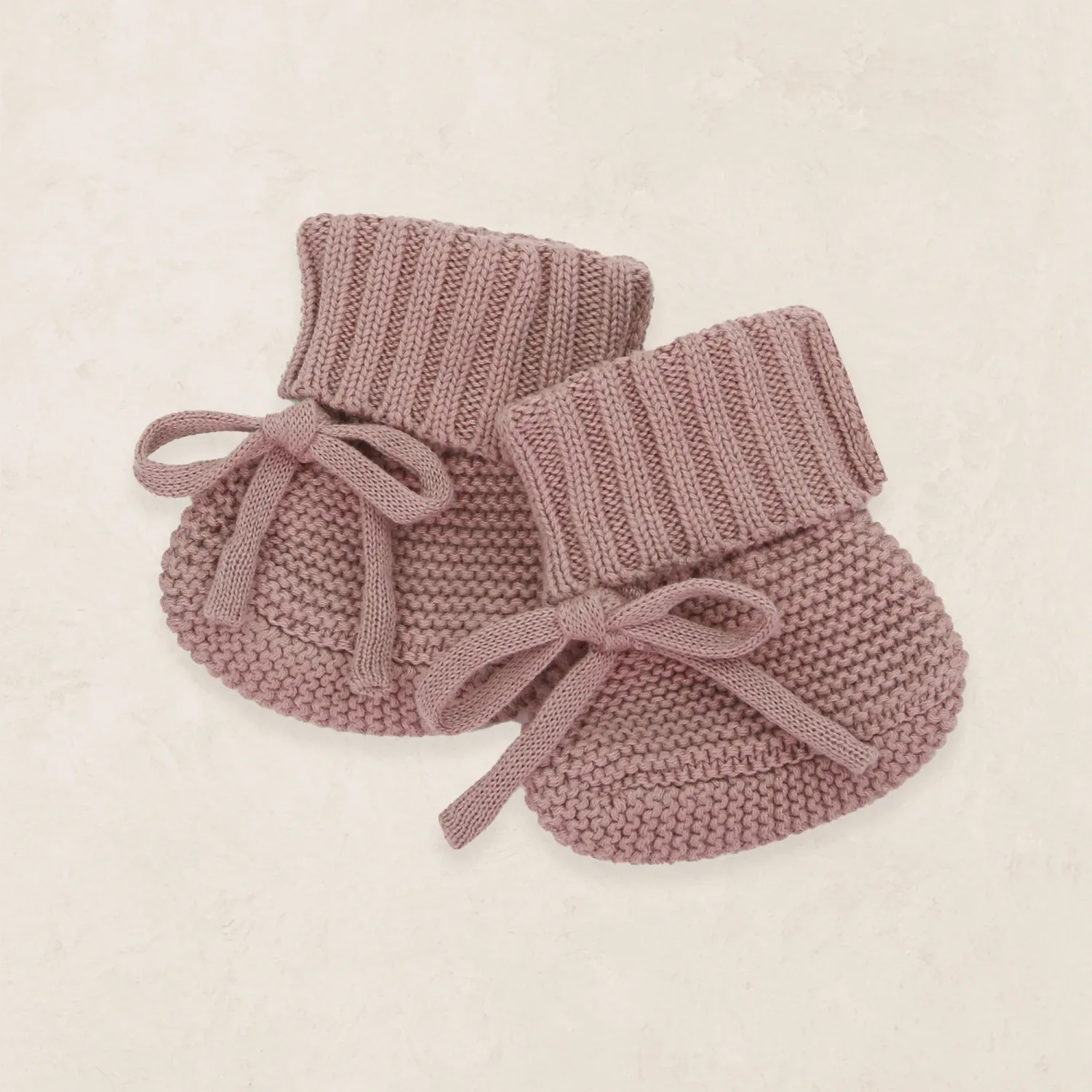 Dusty rose knit baby booties with bow ties displayed on a soft neutral background.
