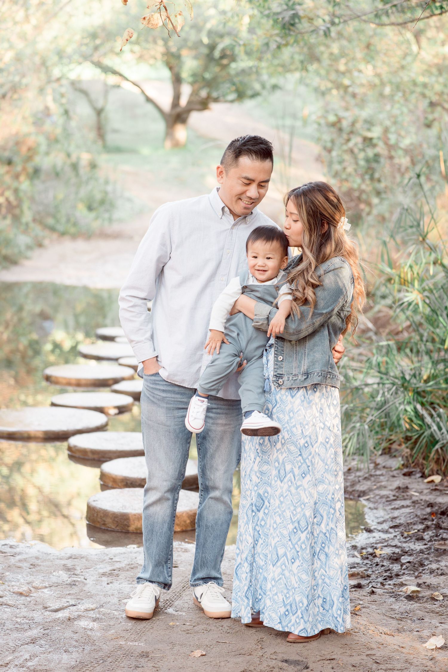 Happy Asian family with laughing baby boy posing on a scenic stepping stone garden path.