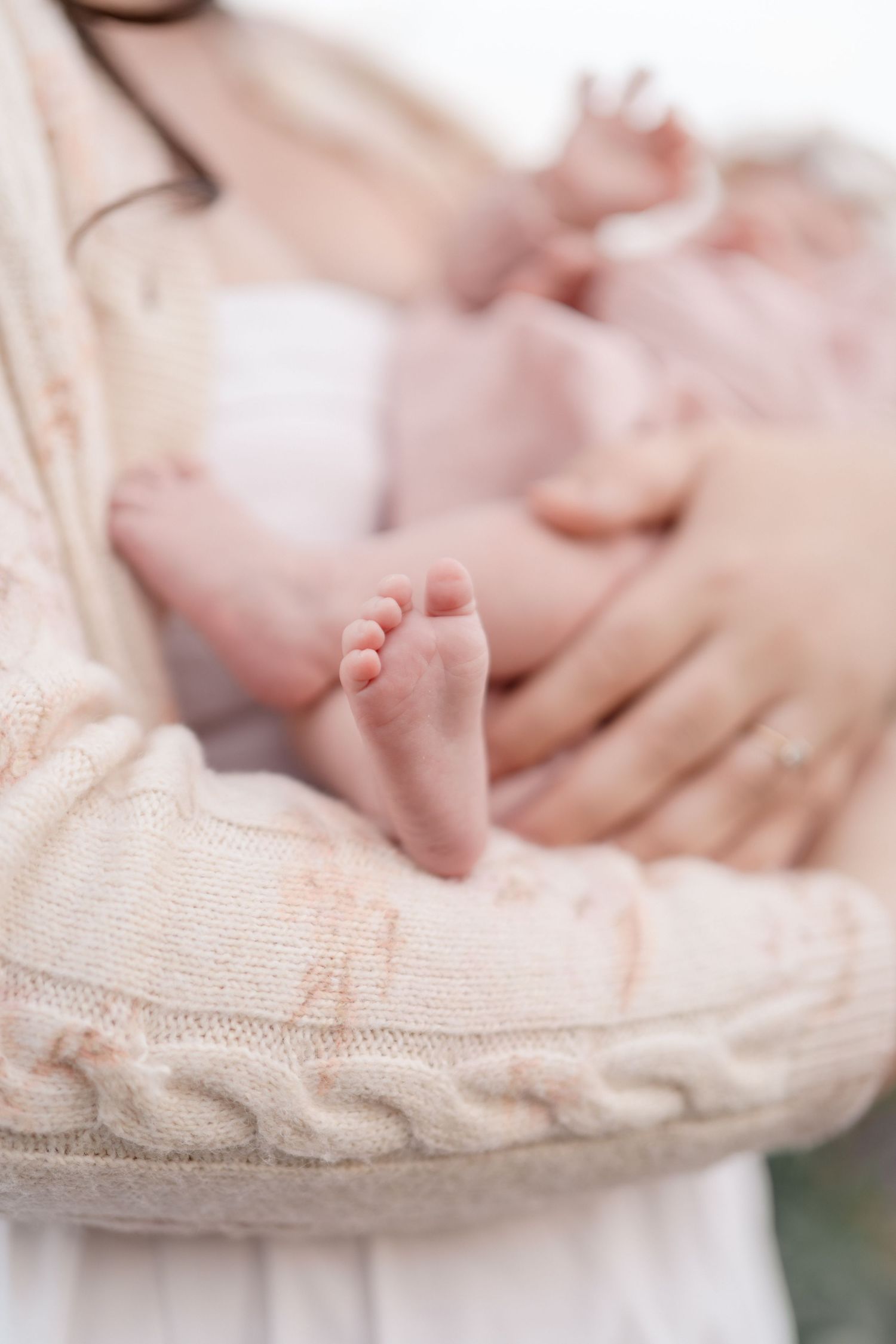 Tiny newborn baby feet rest delicately in a mother's arms during an outdoor newborn photo session.