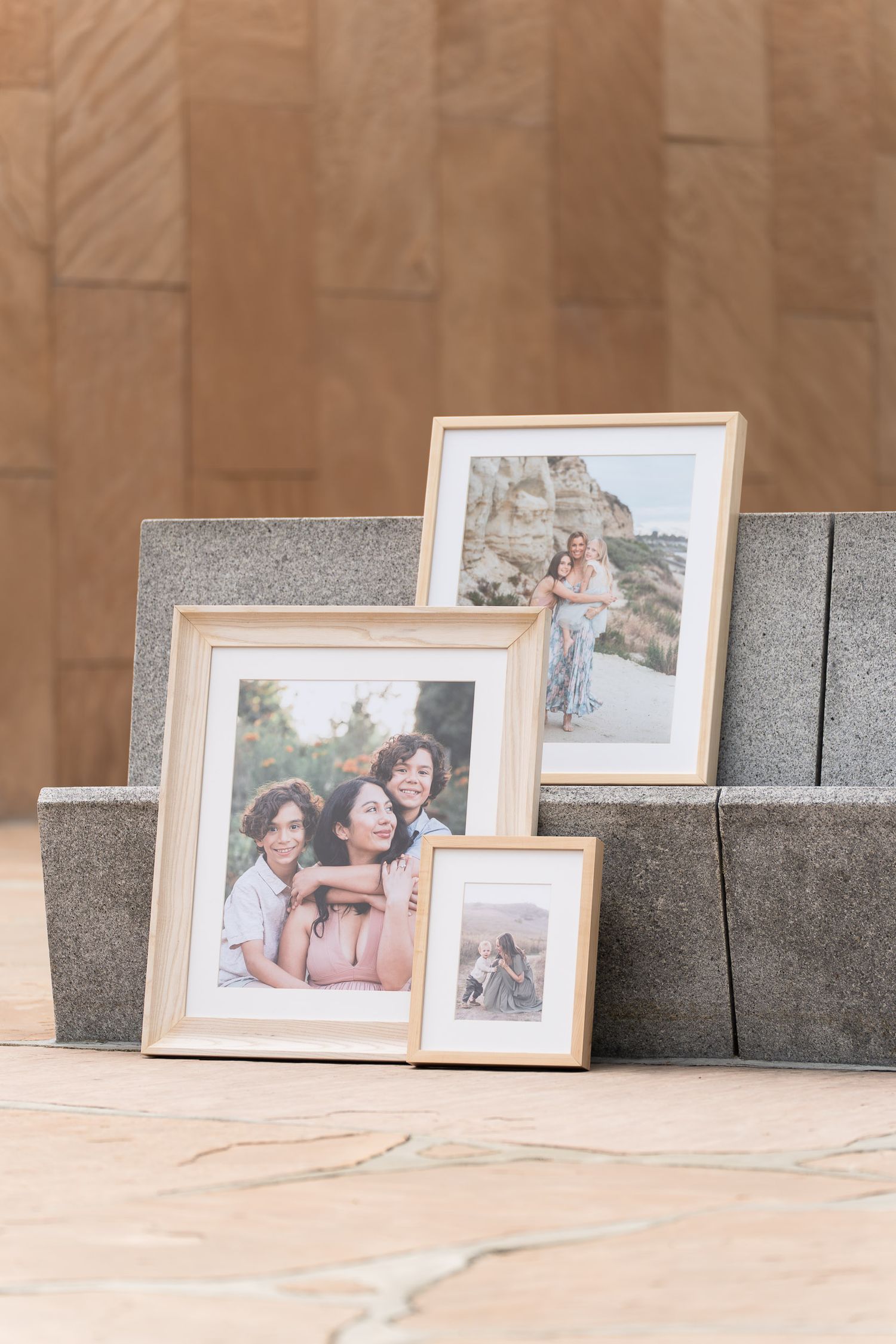 Three gold-framed family photos of women leaning against stone steps with a wood panel wall backdrop.