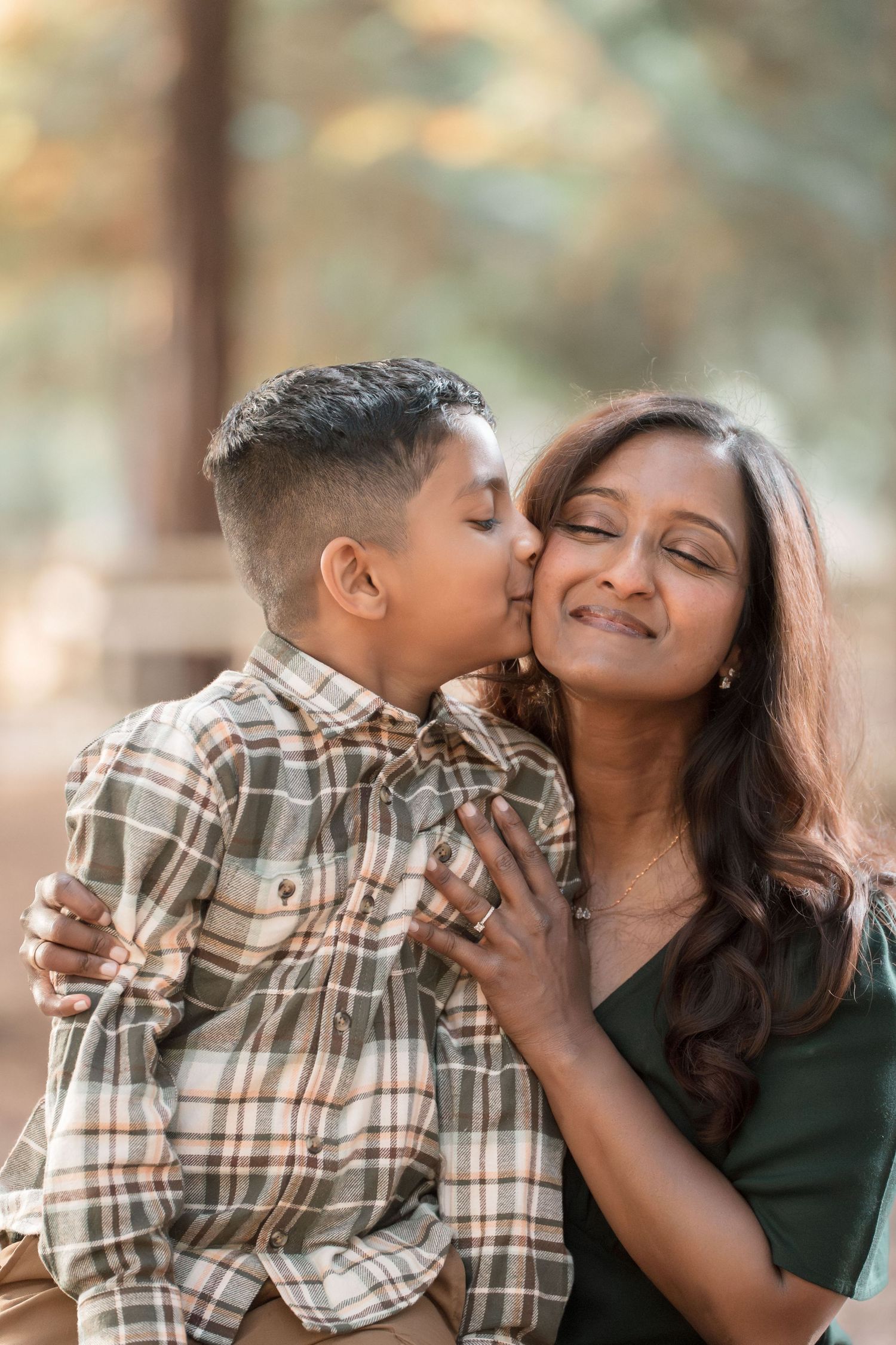 A young boy gives his smiling mother a sweet kiss on the cheek outdoors.