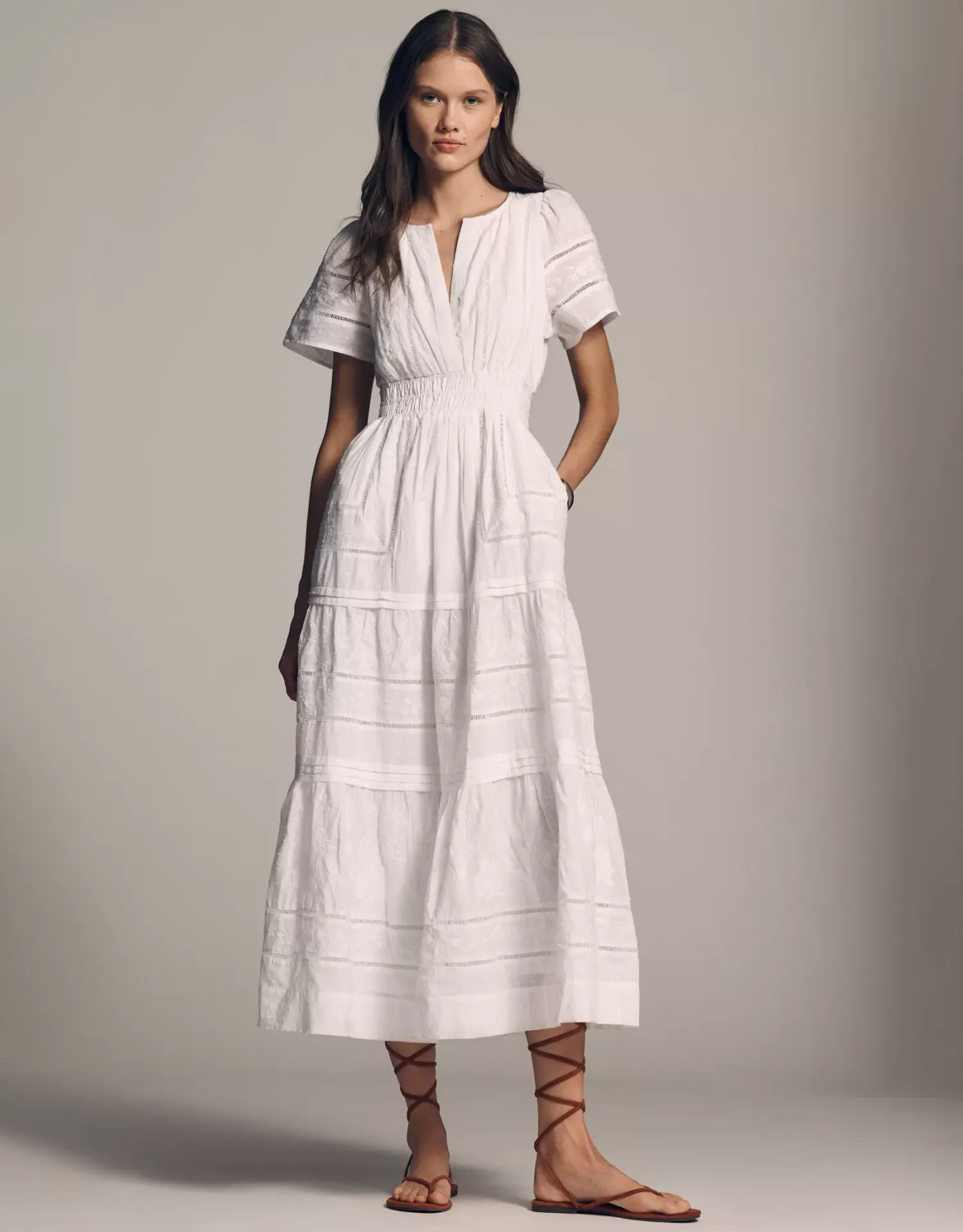 Woman in white tiered midi dress with flutter sleeves and smocked waist, paired with strappy sandals.
