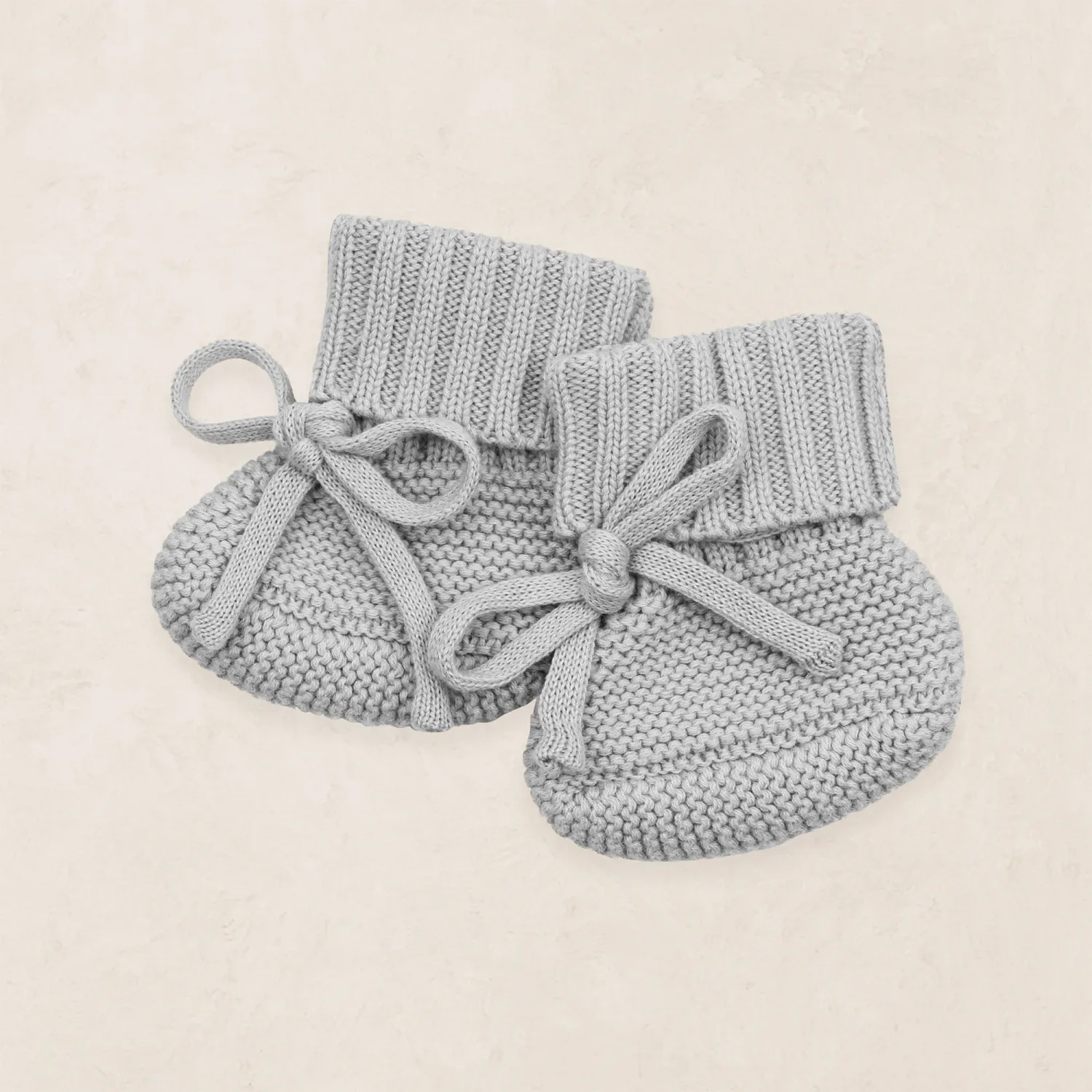 Soft gray knit baby booties with delicate bow ties displayed on a neutral background.
